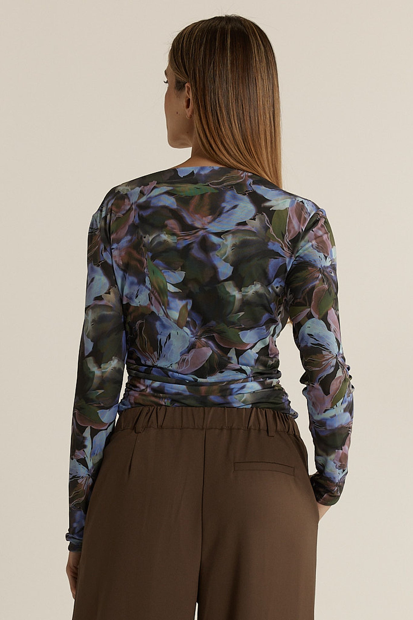 Woman wearing a long-sleeve floral top and brown pants on a beige background