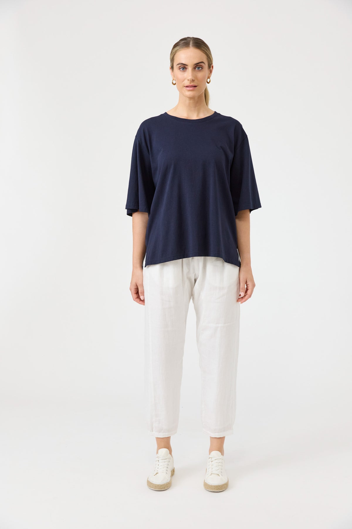 Woman wearing a navy blue top and white pants on a white background