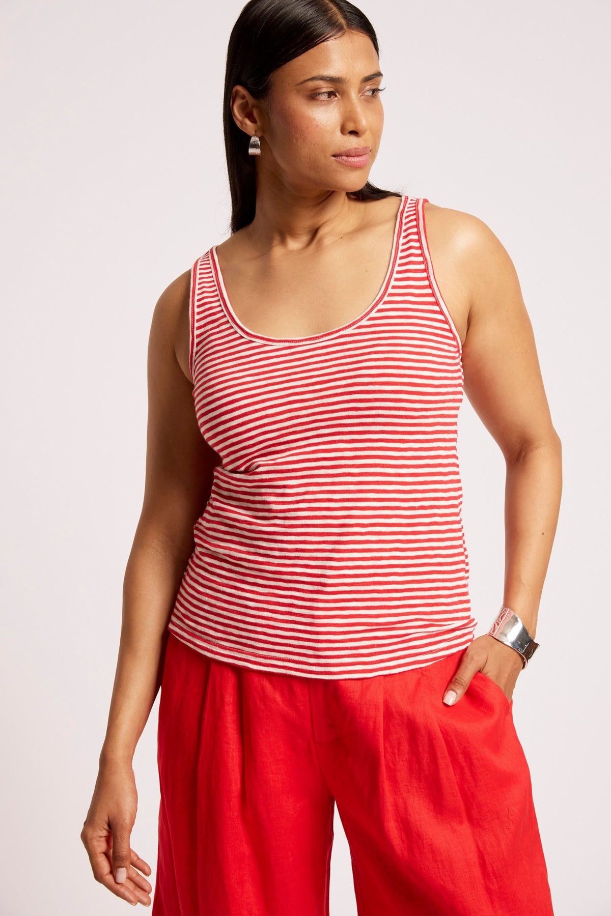 A woman wearing a red and white horizontally striped tank top and bright red wide-leg pants, photographed against a light gray studio background.