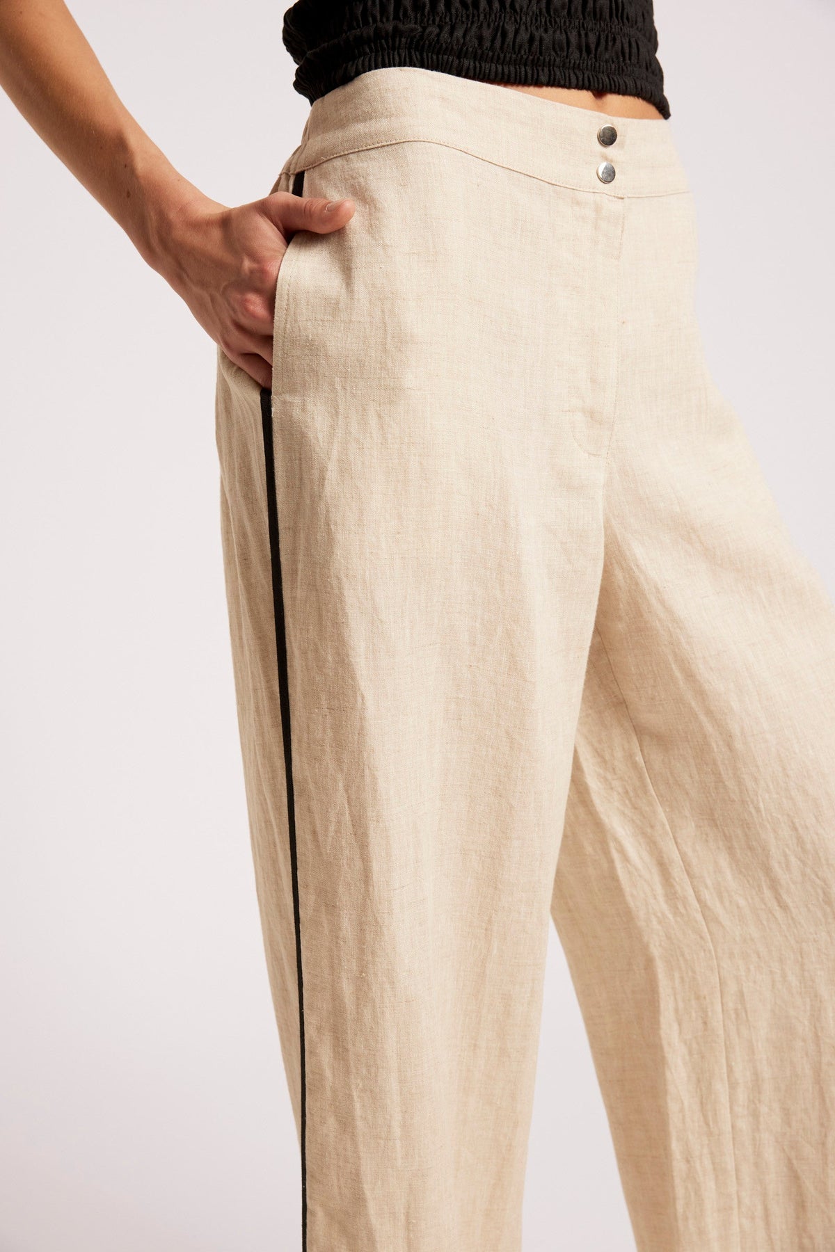 Beige wide-leg linen trousers with a black side stripe, shown on a model from the waist down against a light gray background.