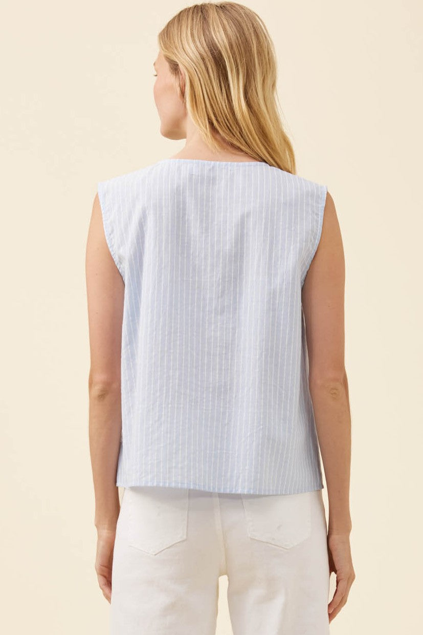 A woman shown from the back wearing a light blue and white vertically striped sleeveless top and white pants, set against a solid cream background.