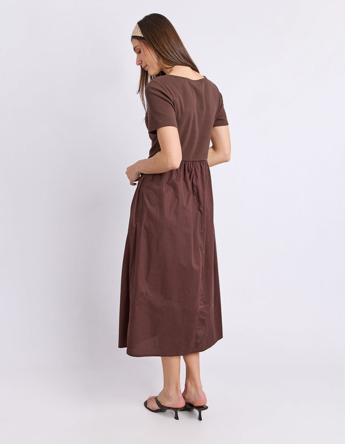 A woman modeling a brown short-sleeve midi dress from the back, standing against a plain light gray studio background.