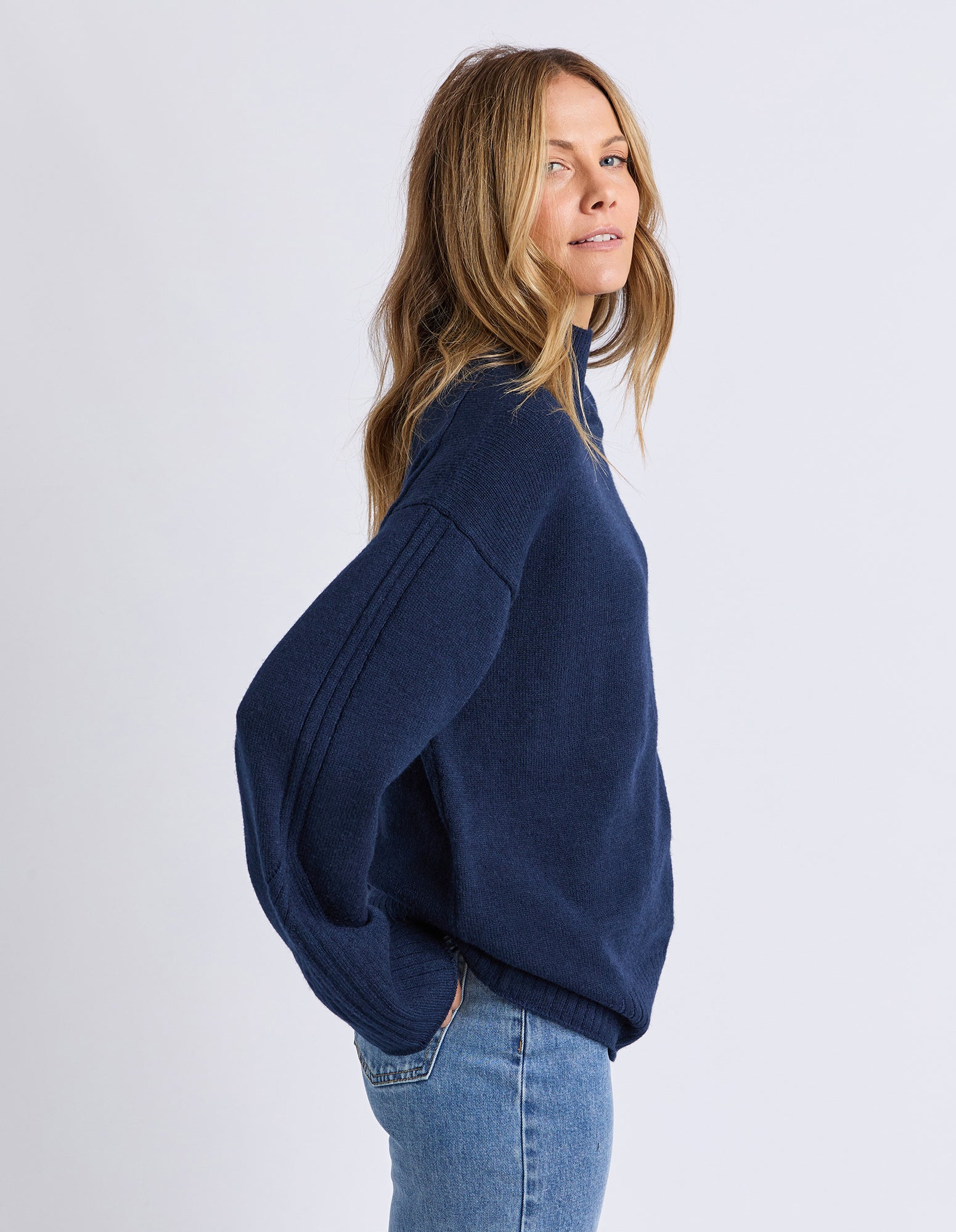 Woman wearing a navy sweater and jeans on a white background