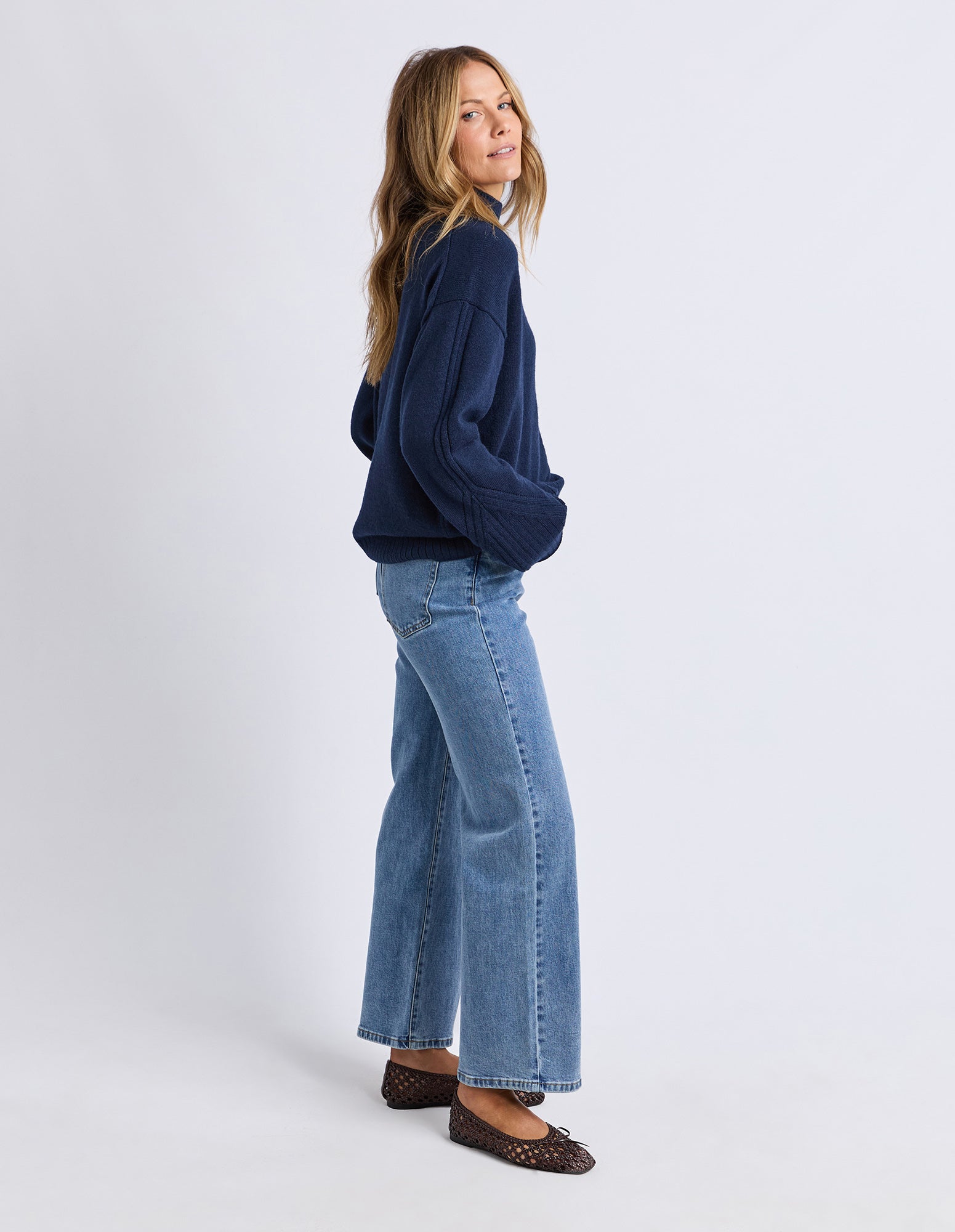 Woman wearing a navy sweater and light blue jeans on a white background