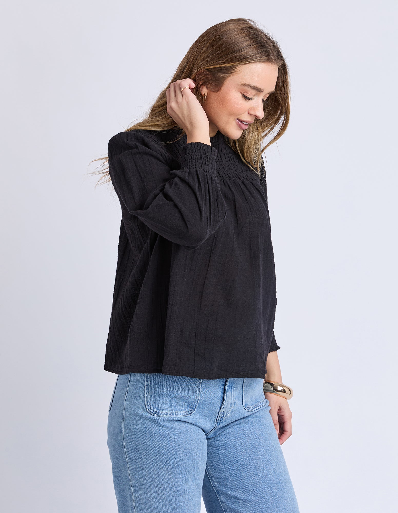 Woman wearing a black top and blue jeans on a light gray background