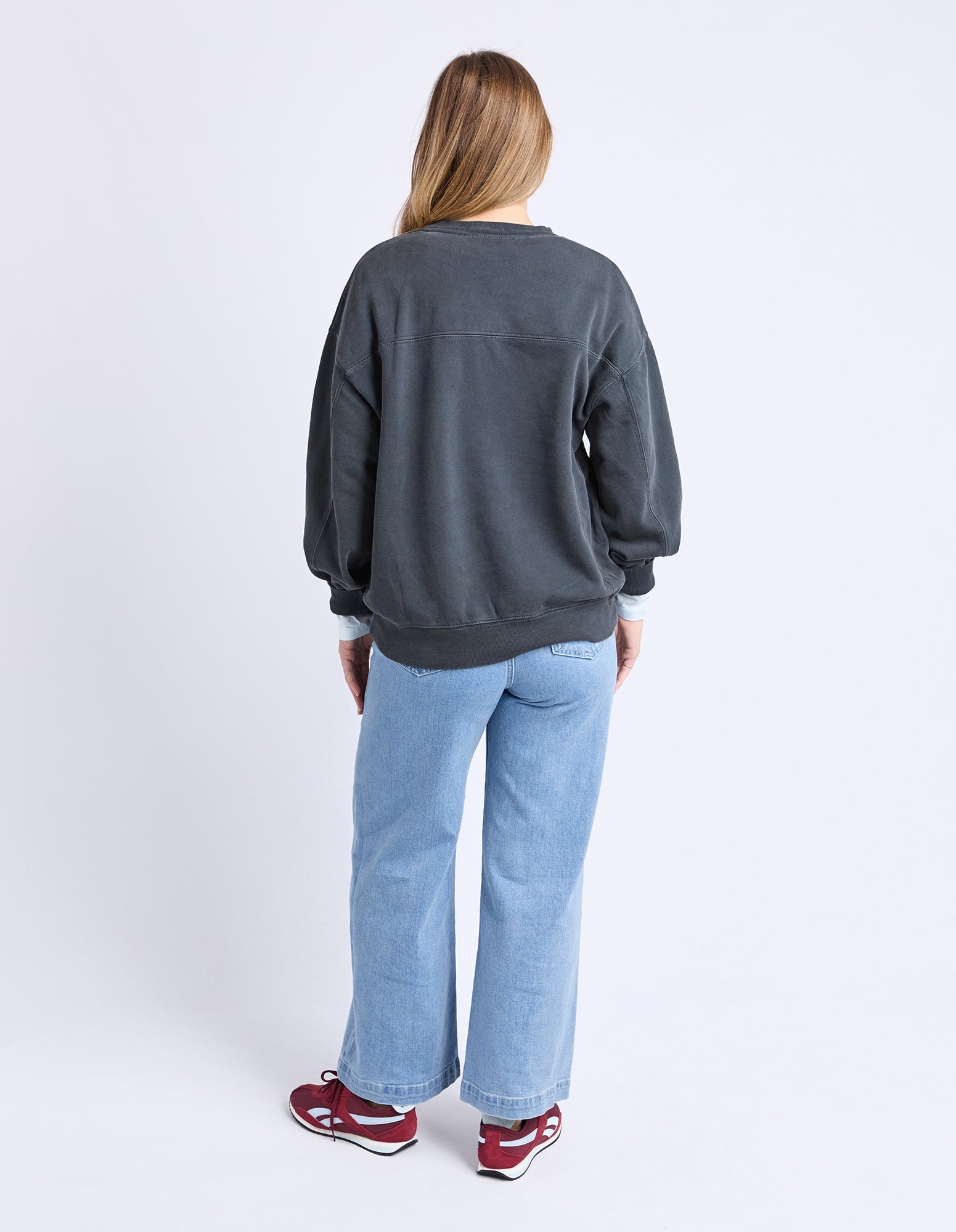 Person wearing a dark gray sweatshirt and light blue jeans on a white background