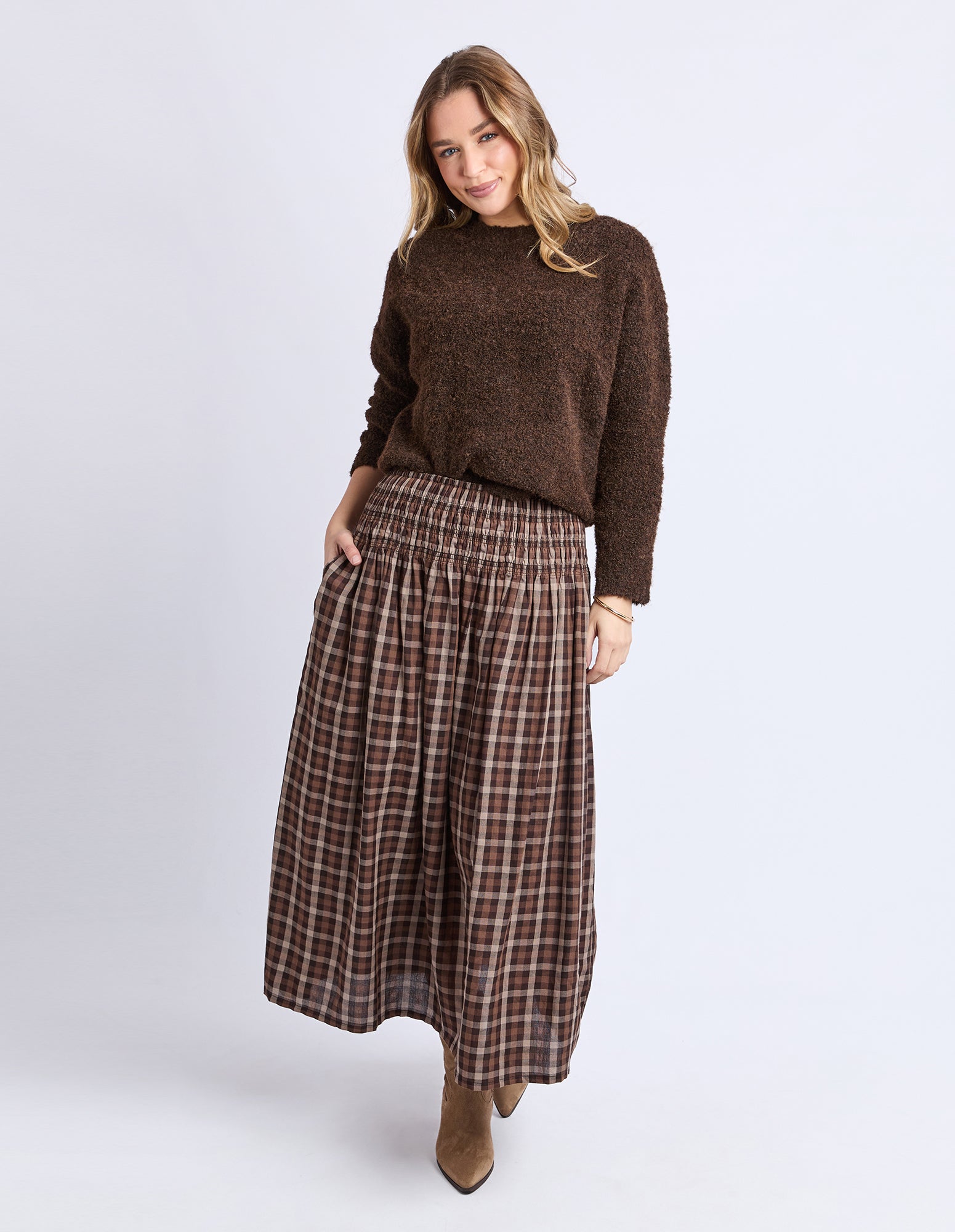 Woman wearing a brown sweater and plaid skirt on a white background