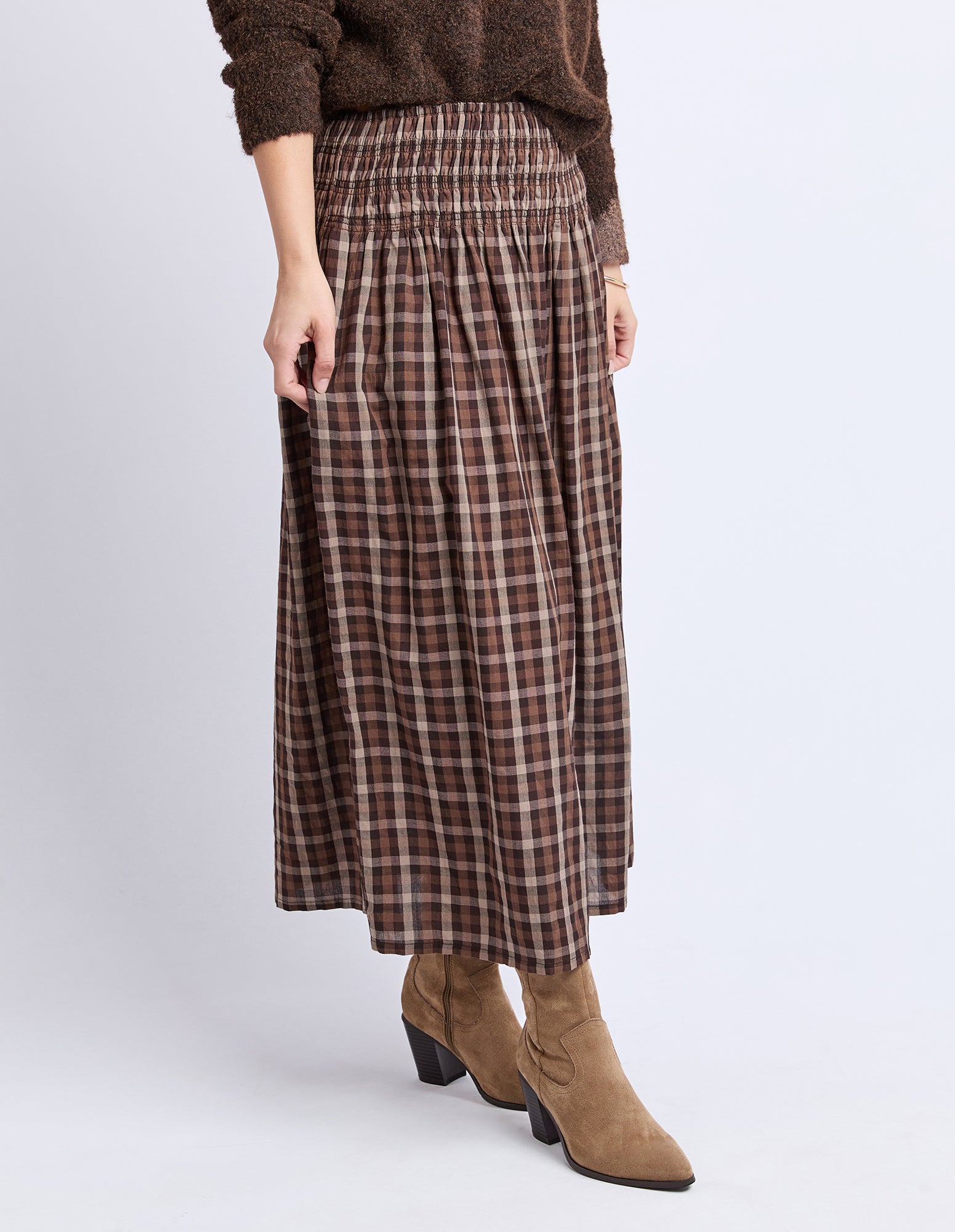 Person wearing a plaid skirt and brown sweater on a white background