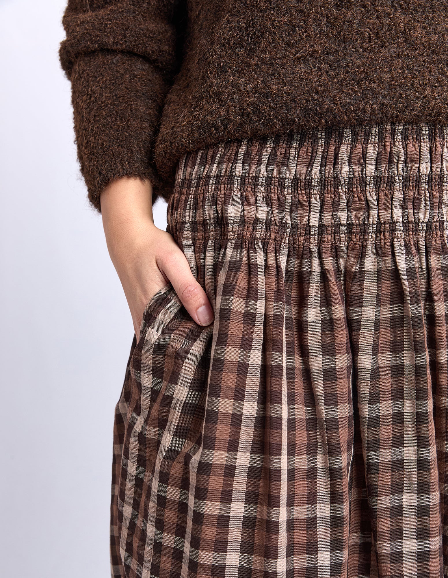 Brown plaid pants worn with a brown sweater on a light gray background