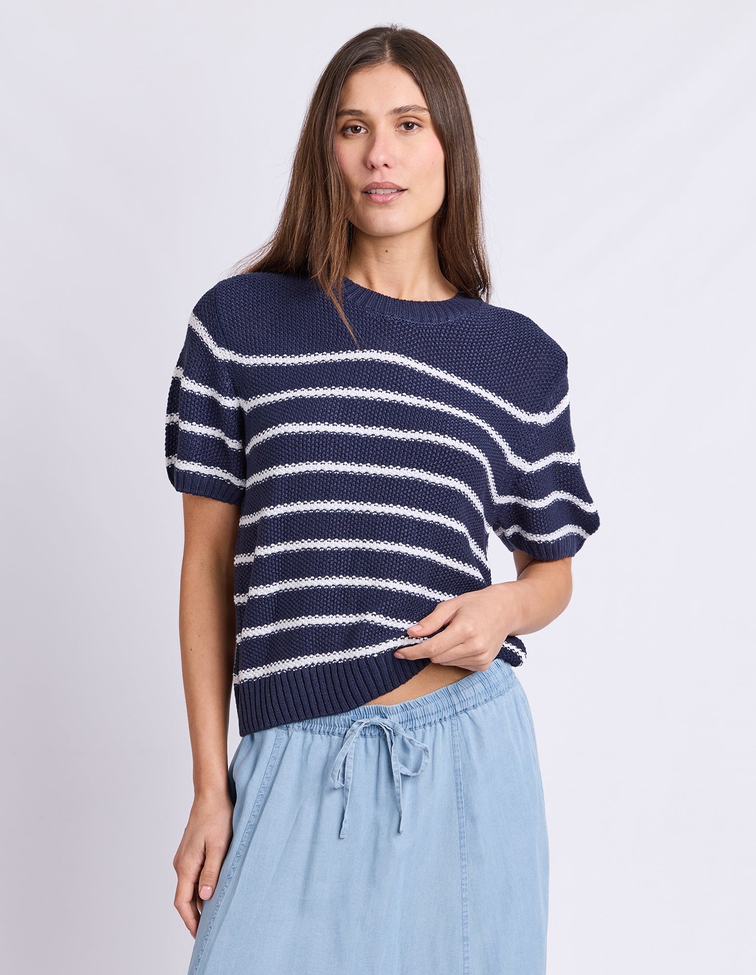 A woman modeling a navy blue short-sleeve knit top with white horizontal stripes, paired with light blue drawstring pants, against a light gray studio background.