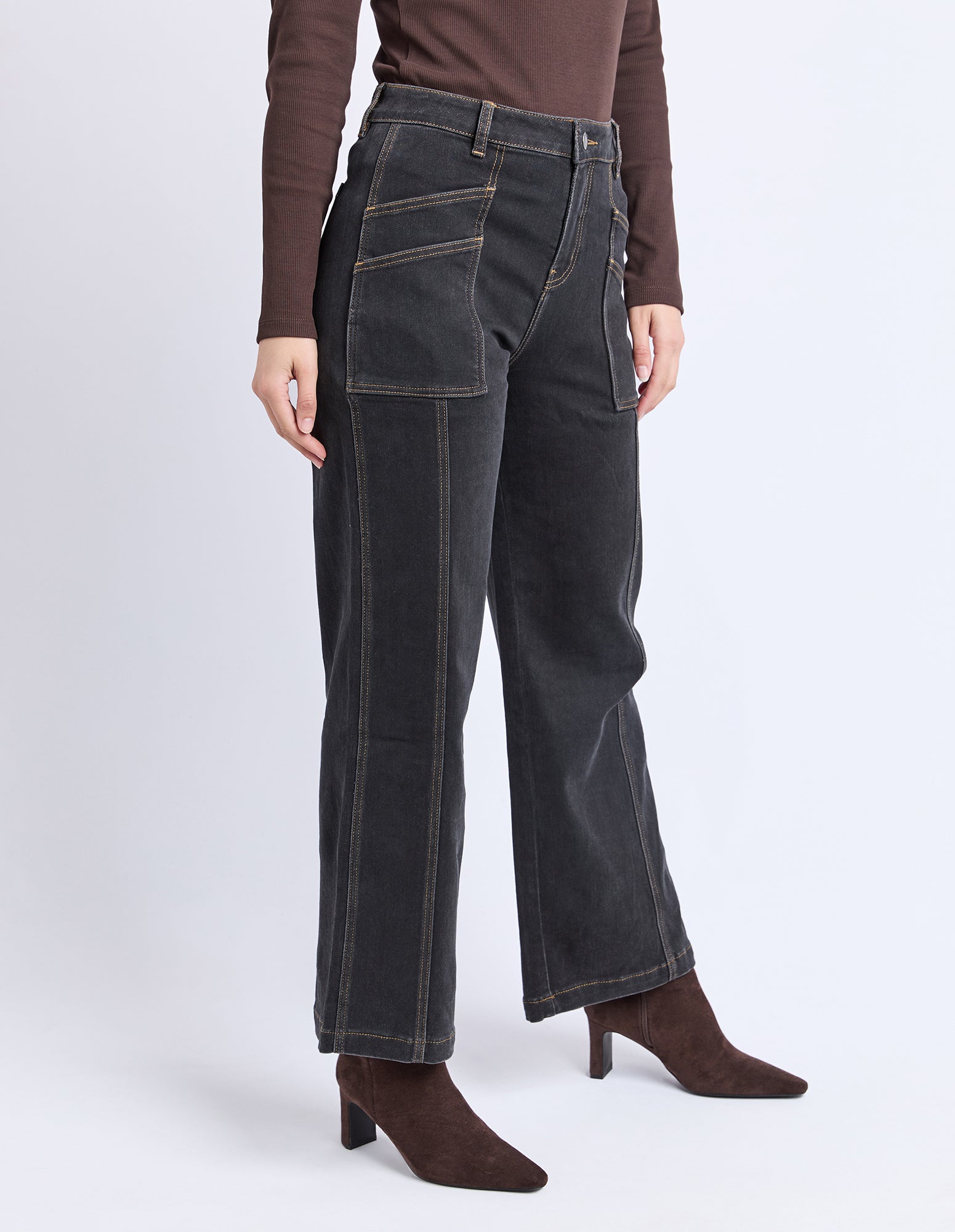 Person wearing dark gray jeans and brown shoes on a white background