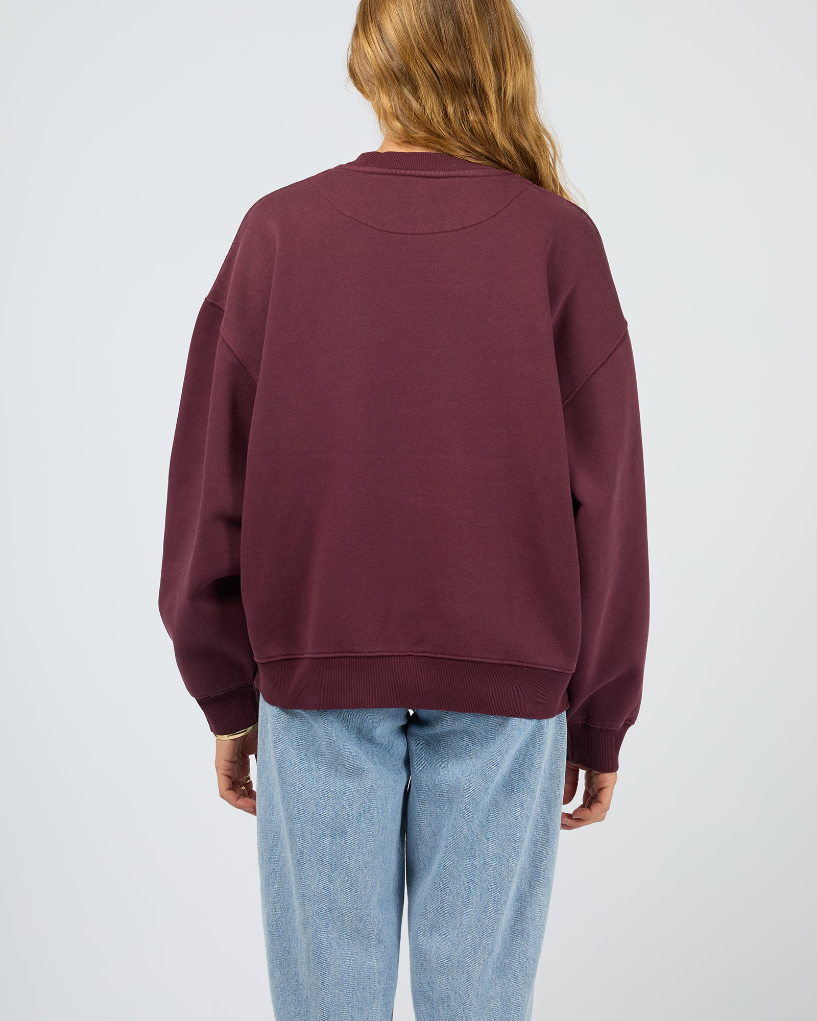 Person wearing a maroon sweatshirt and light blue jeans on a plain background