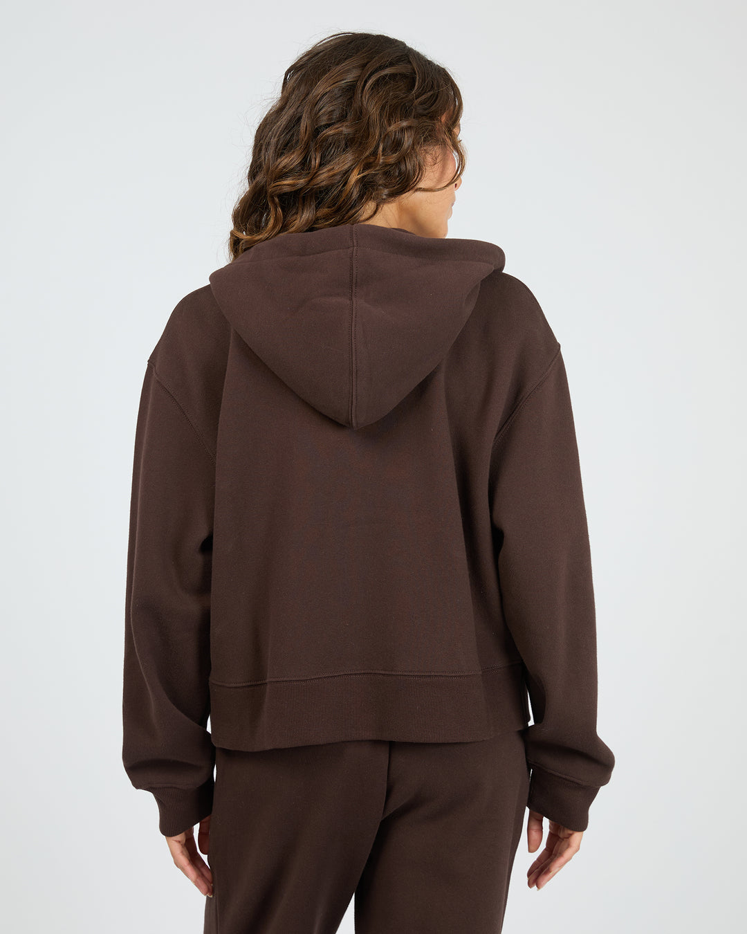 Person wearing a brown hoodie and pants on a white background