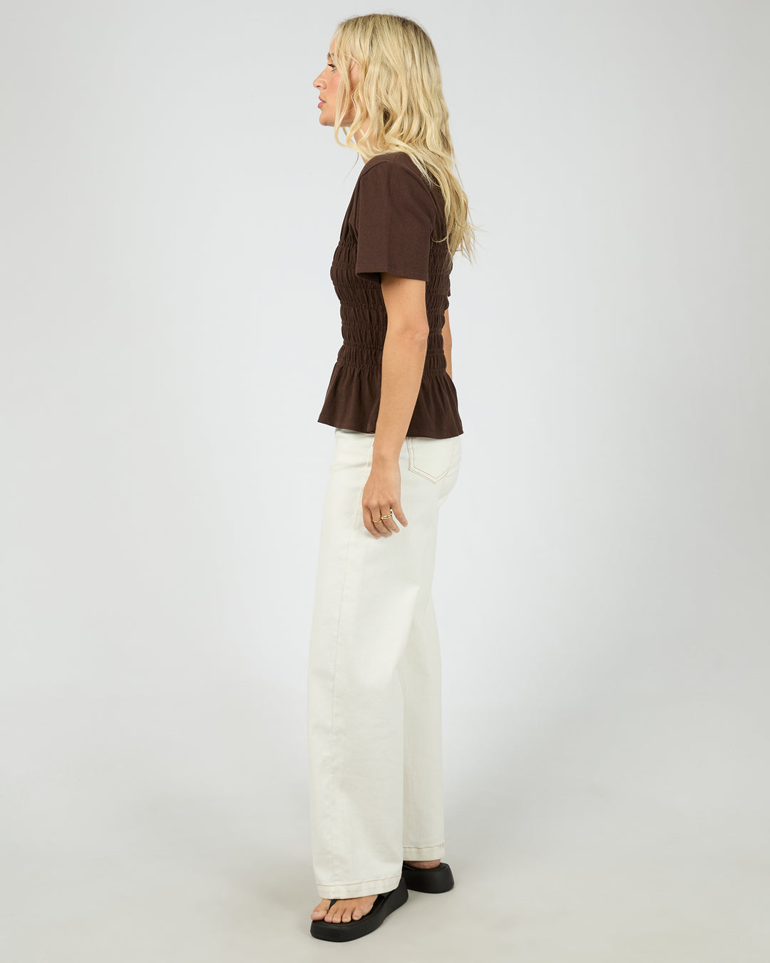 Woman wearing a brown top and white pants on a plain background
