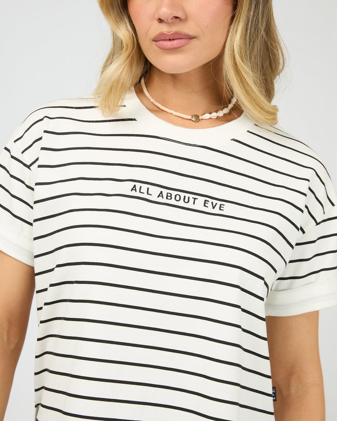 A close-up of a woman wearing a white short-sleeve t-shirt with thin black horizontal stripes and the text 'ALL ABOUT EVE' printed across the chest.