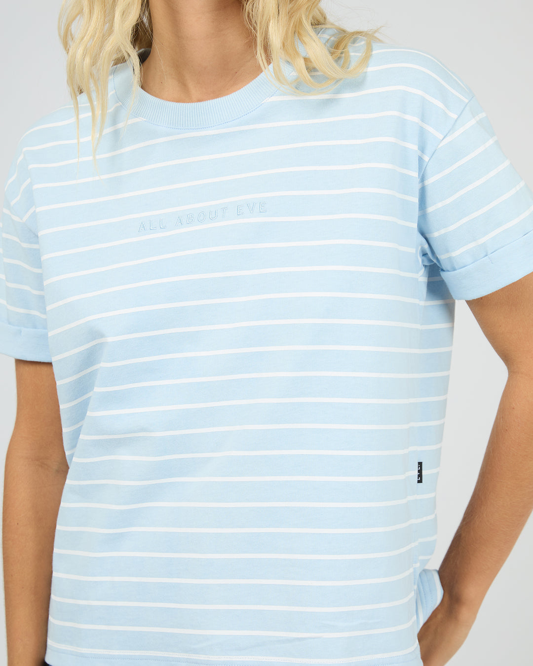 A close-up of a model wearing a light blue and white horizontally striped t-shirt with 'ALL ABOUT EVA' printed in a subtle tone on the chest.