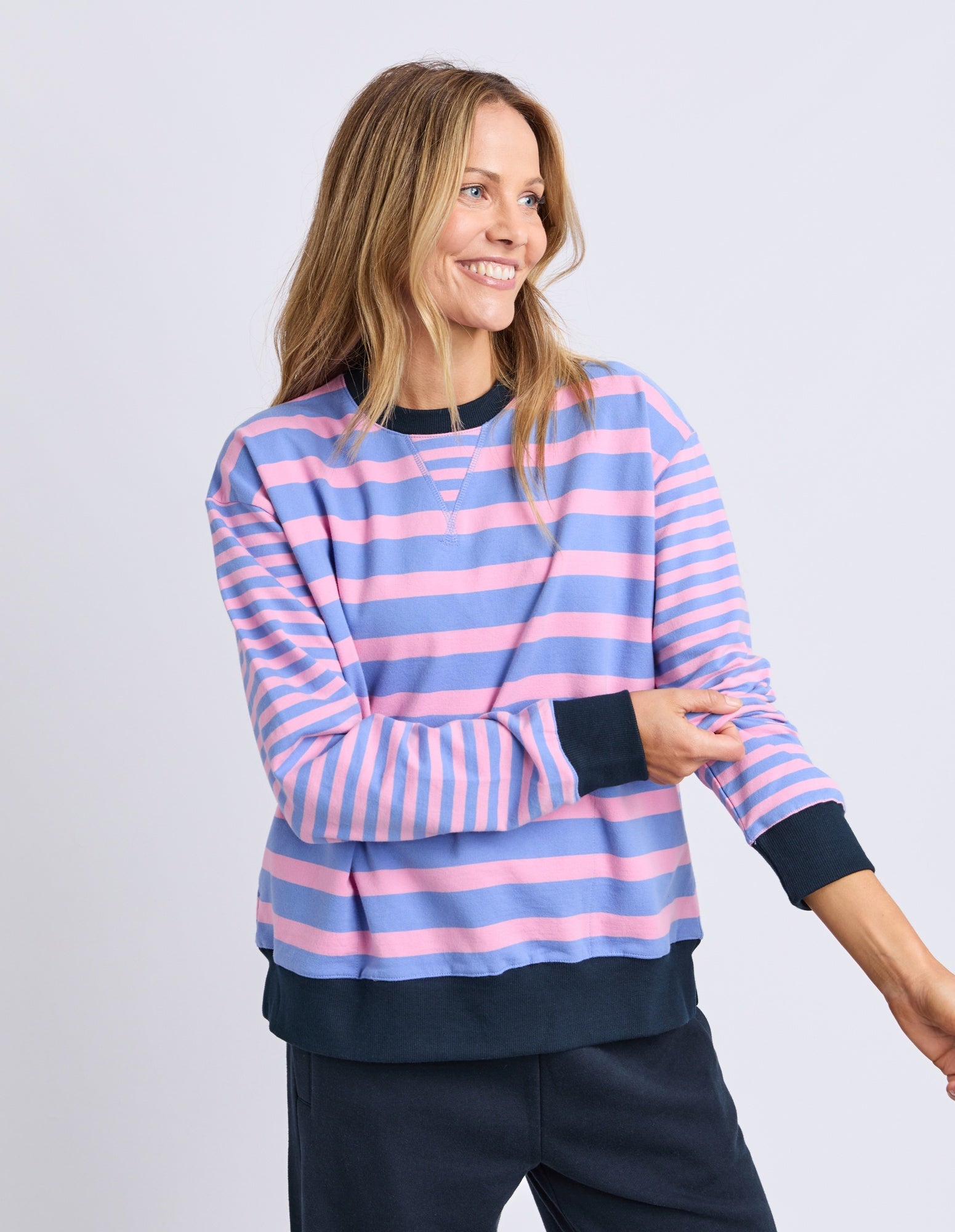 Woman wearing a striped sweater with pink and blue horizontal stripes on a plain background