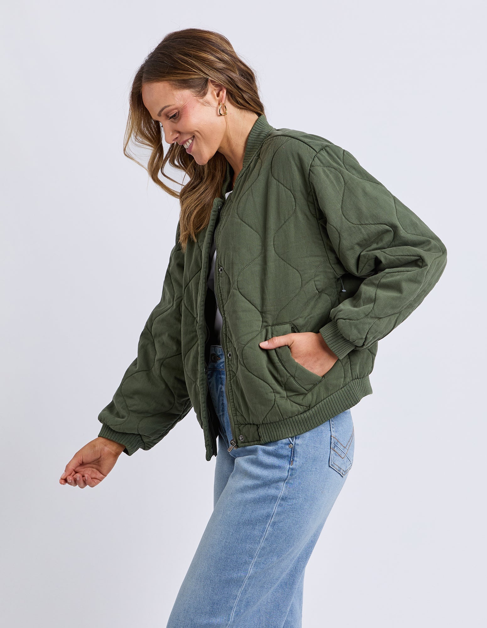 Woman wearing a green quilted jacket and blue jeans on a light gray background