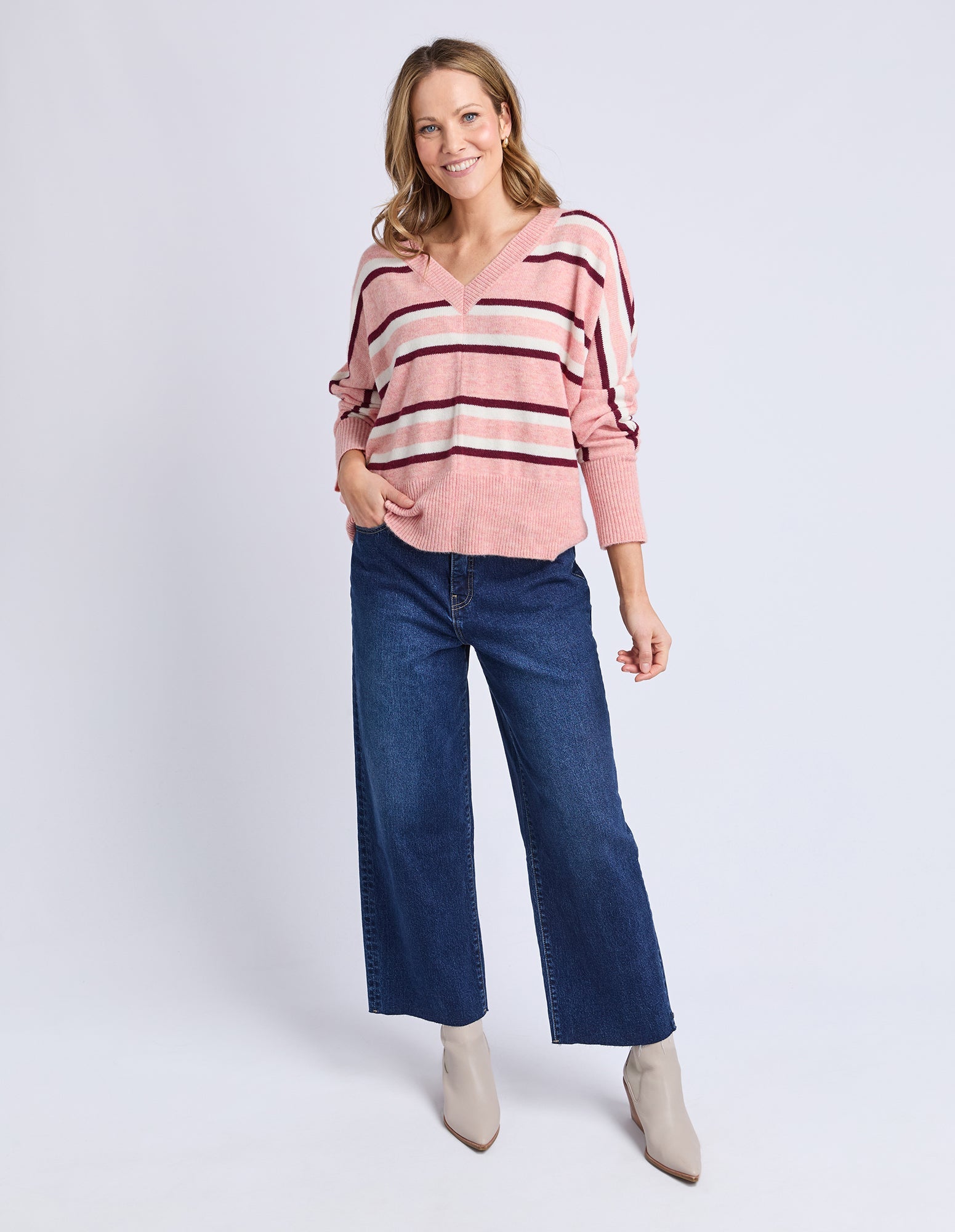 Woman wearing a pink striped sweater and blue jeans on a white background