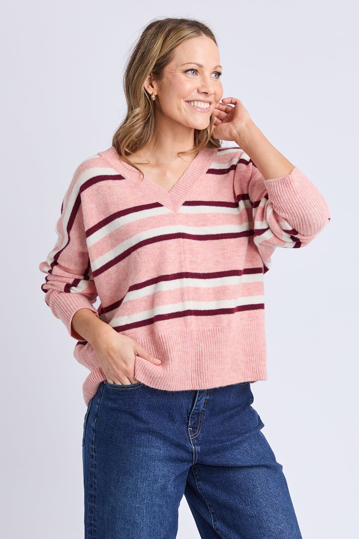 Woman wearing a pink and red striped sweater with blue jeans on a light gray background