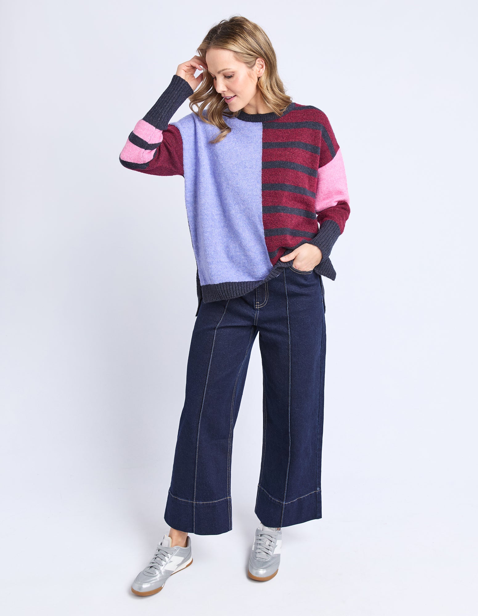 Woman wearing a colorful sweater and blue jeans on a white background