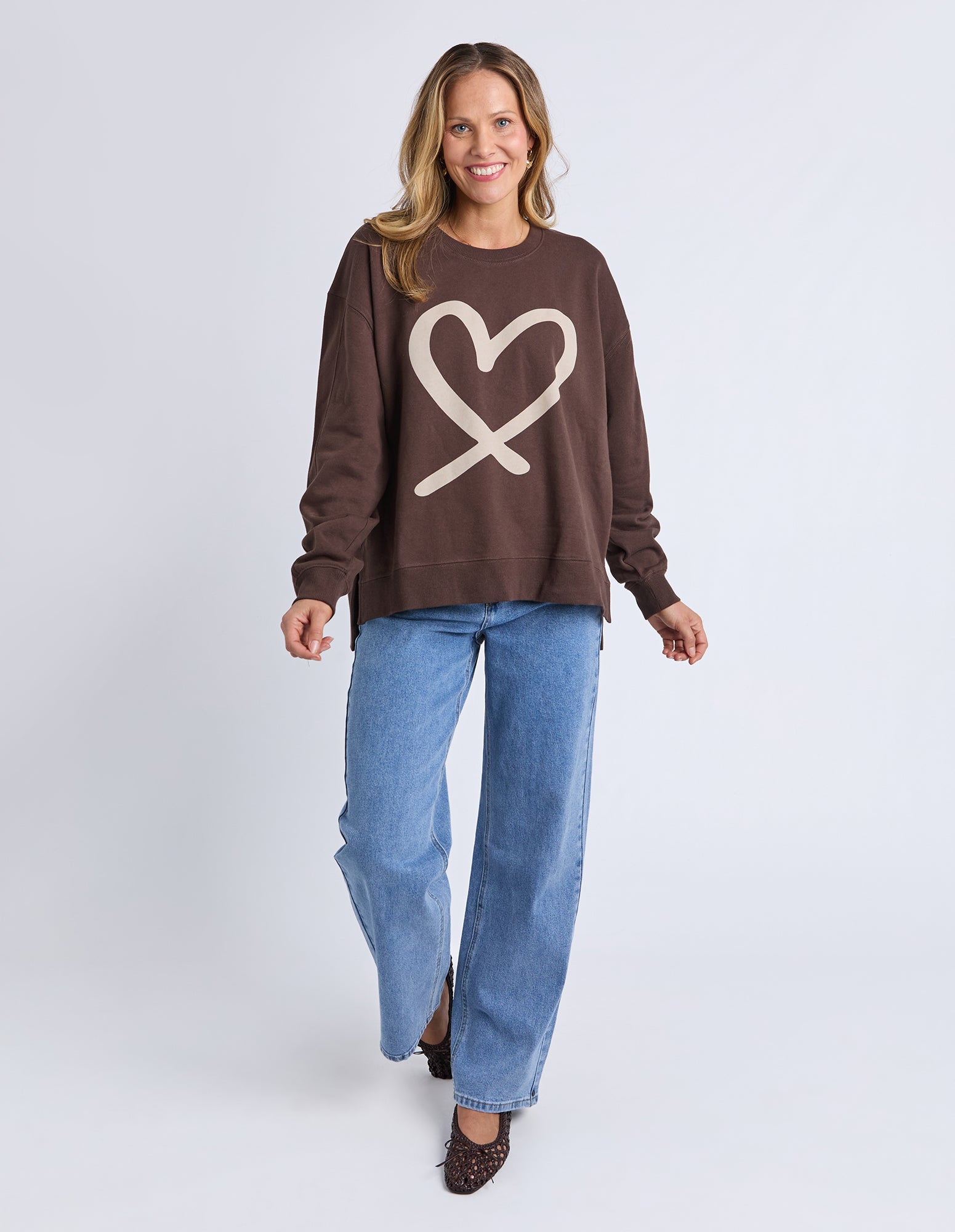 Woman wearing a brown sweatshirt with a heart design and blue jeans on a white background