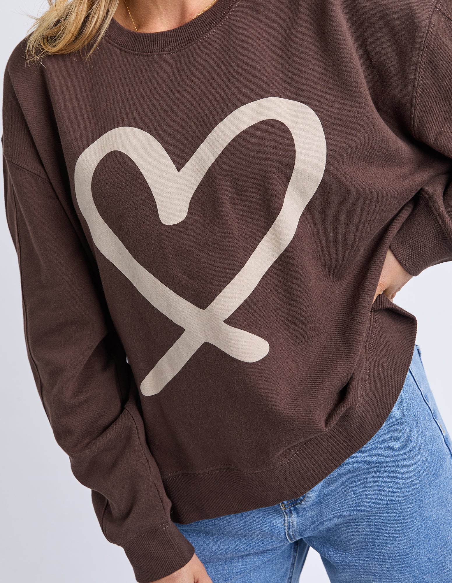 Brown sweatshirt with a beige heart design worn by a person with blue jeans.