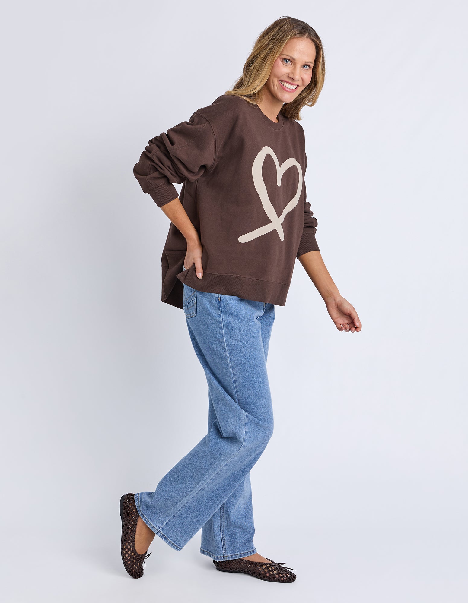 Woman wearing a brown sweatshirt with a heart design and blue jeans on a white background