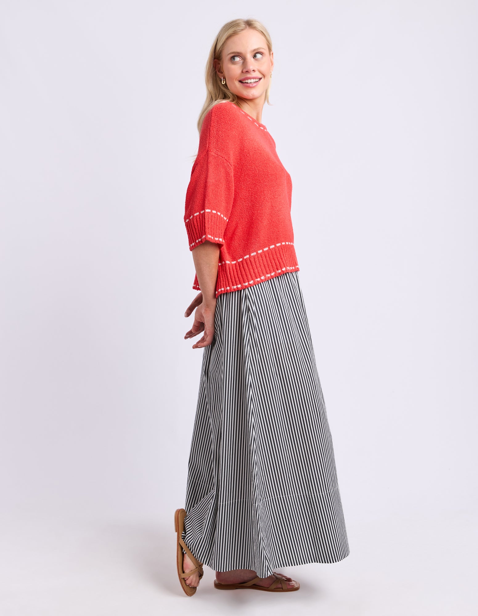 Woman wearing a red sweater and long striped skirt on a white background