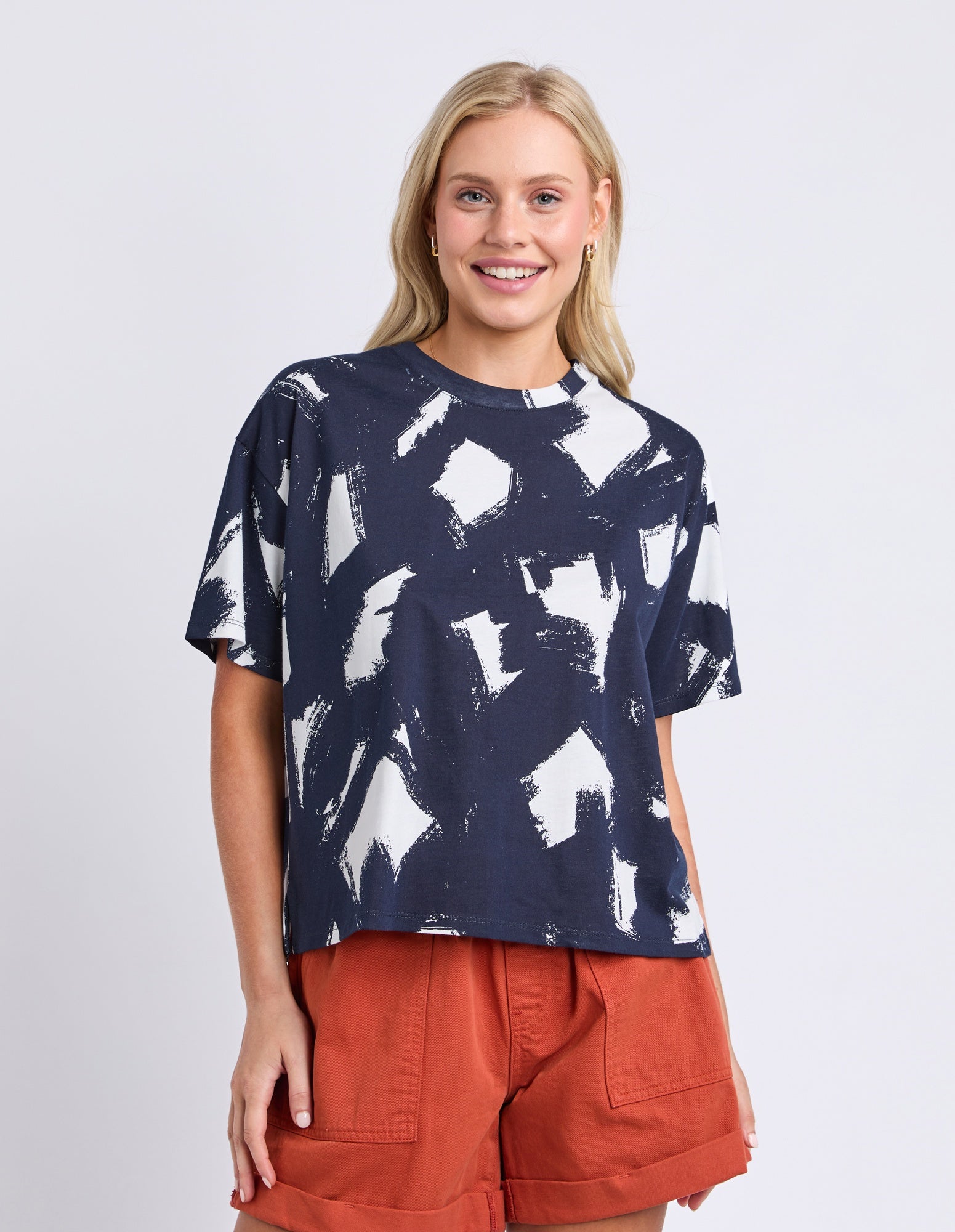 Woman wearing a navy blue t-shirt with white abstract patterns and orange shorts on a light gray background