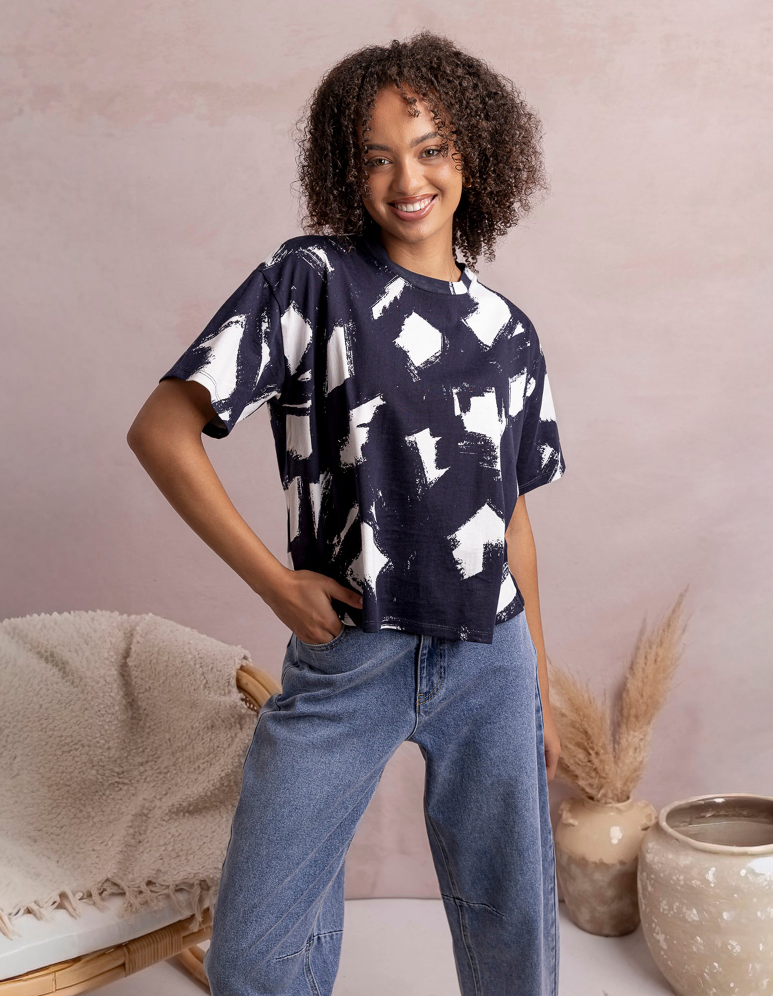 Woman wearing a black and white patterned top and blue jeans standing against a neutral background.