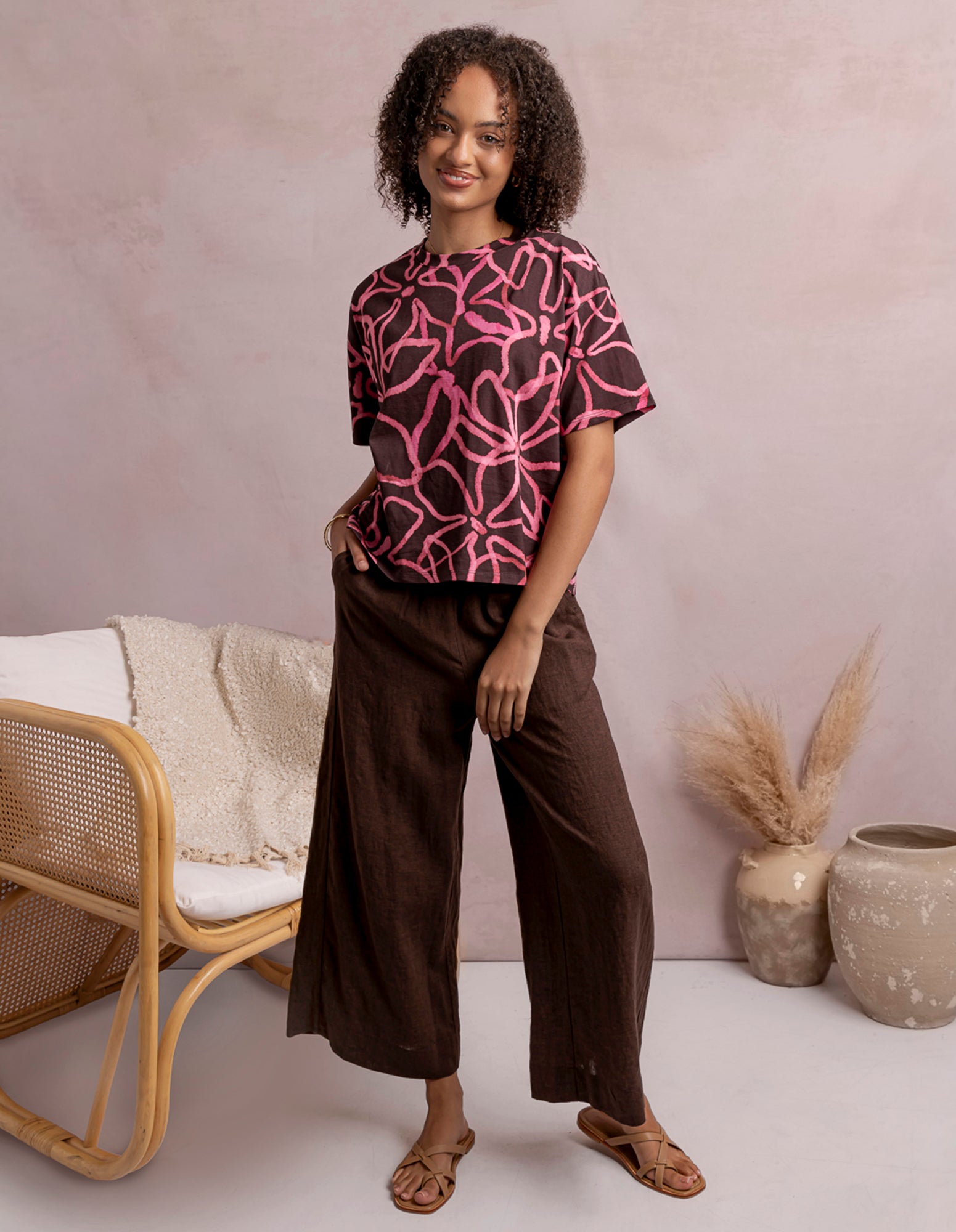 Woman wearing a pink and black patterned top with brown pants in a minimalistic setting.