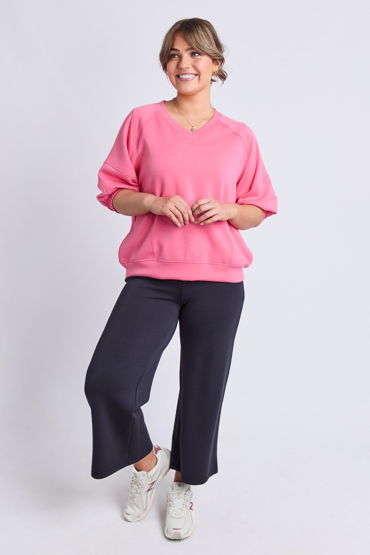 A woman modeling a pink crewneck sweatshirt and dark navy wide-leg pants against a light gray studio background.