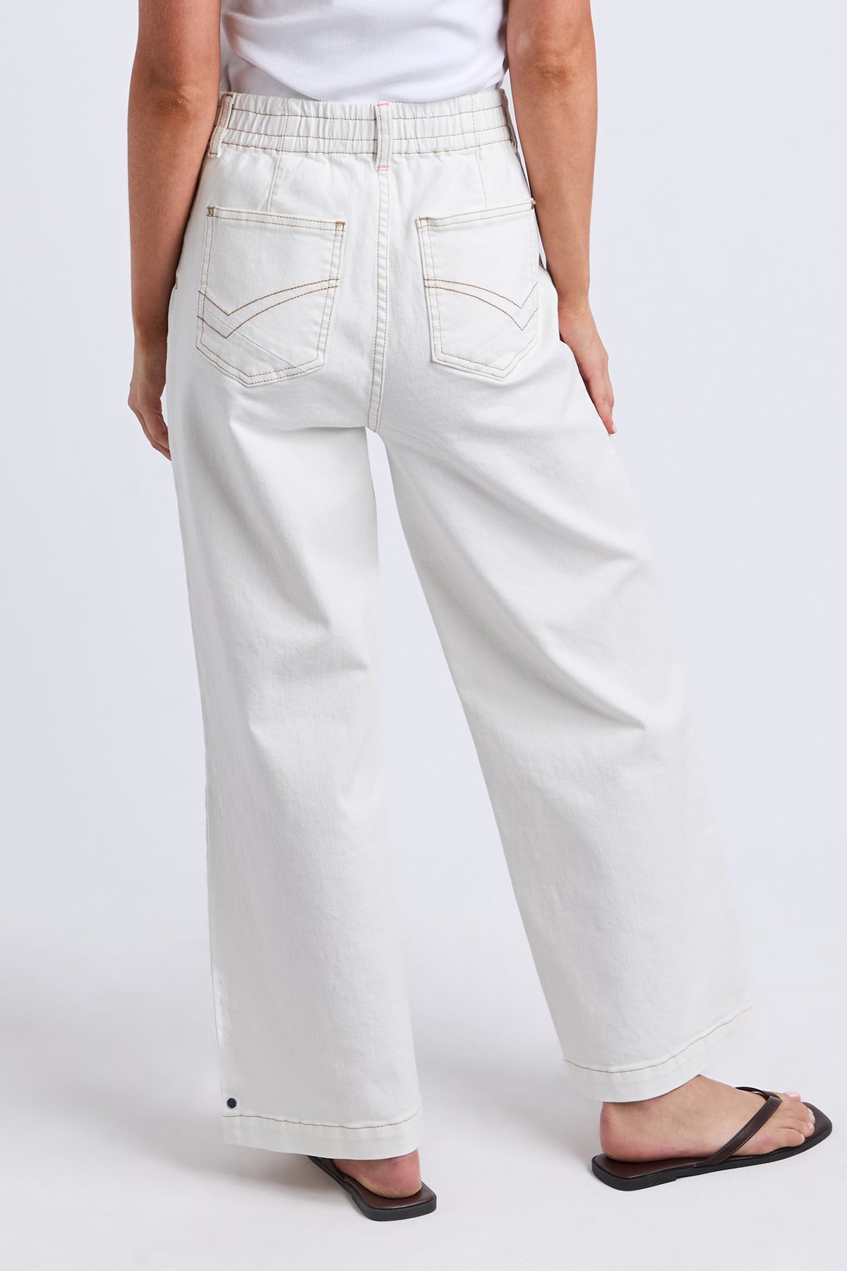 White wide-leg cropped jeans with an elastic waistband, shown from the back on a model wearing black flip-flops against a light gray studio background.