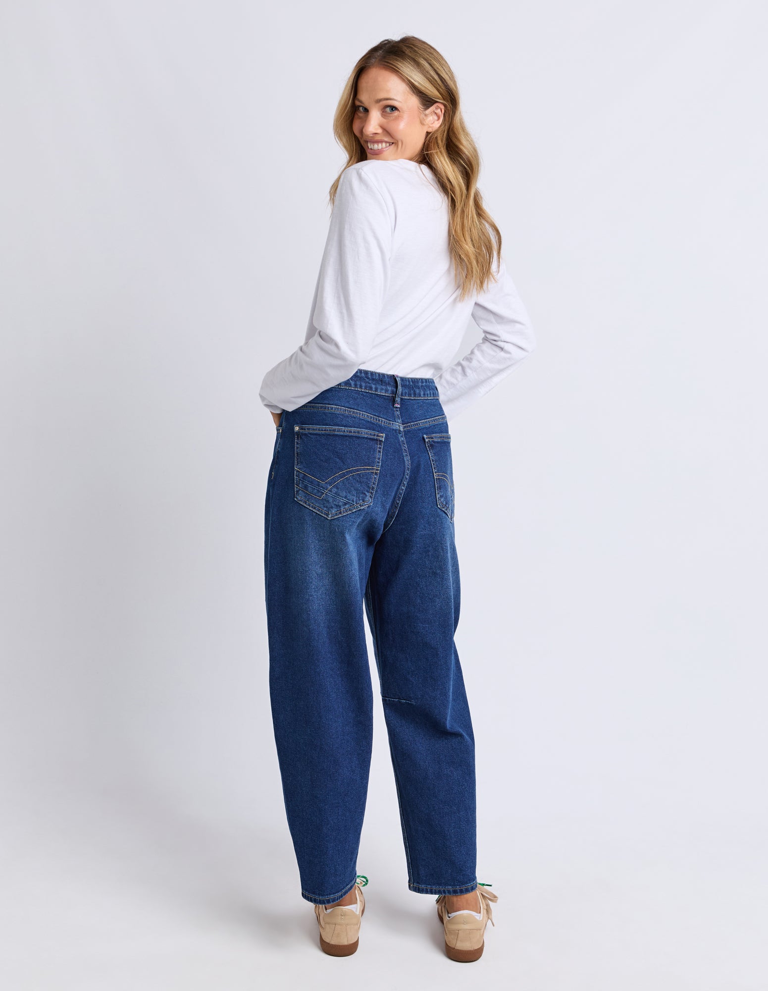 Woman wearing blue jeans and a white shirt on a plain background