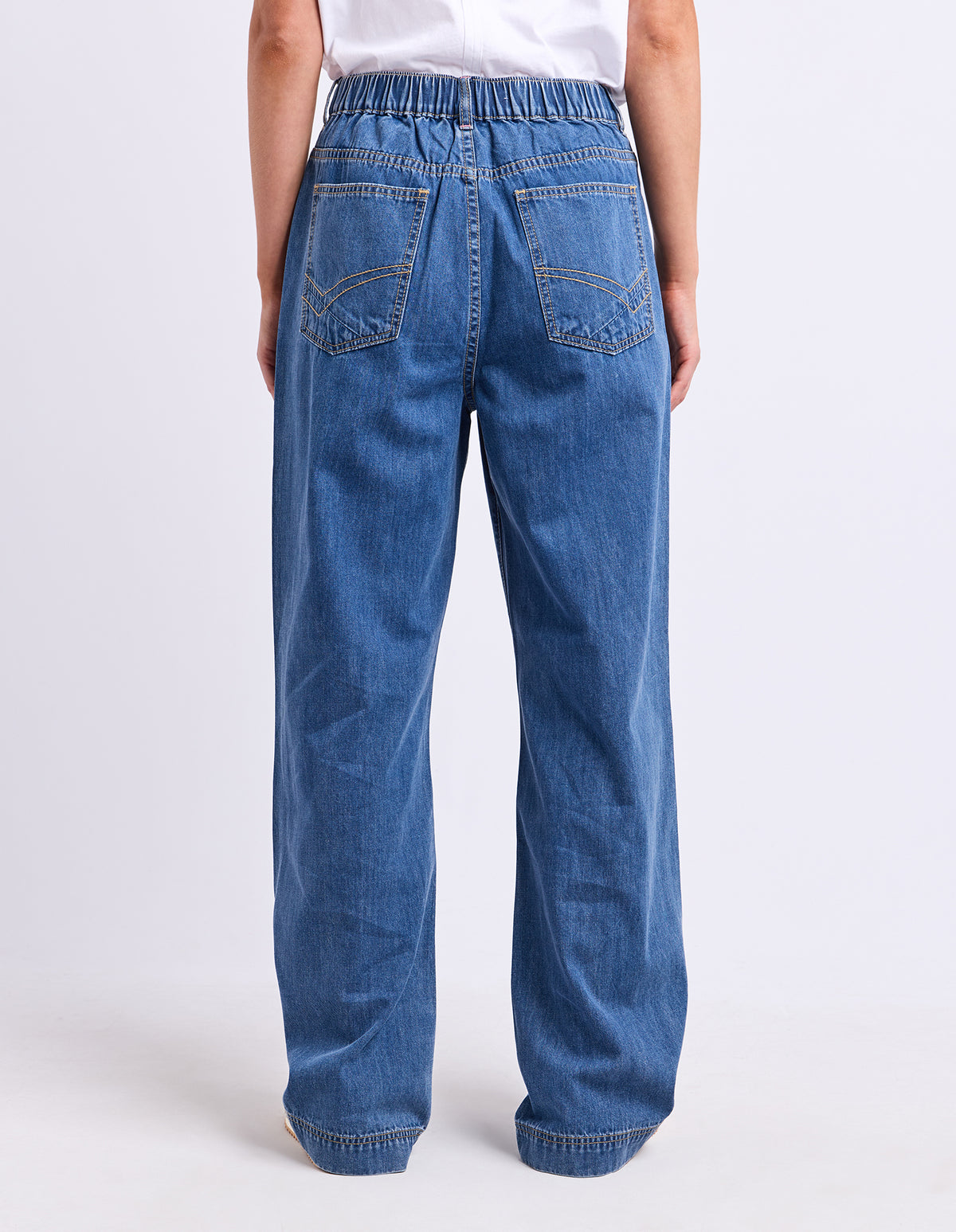 A person shown from the back wearing wide-leg blue denim jeans with an elastic waistband and back pocket details, against a plain light gray studio background.