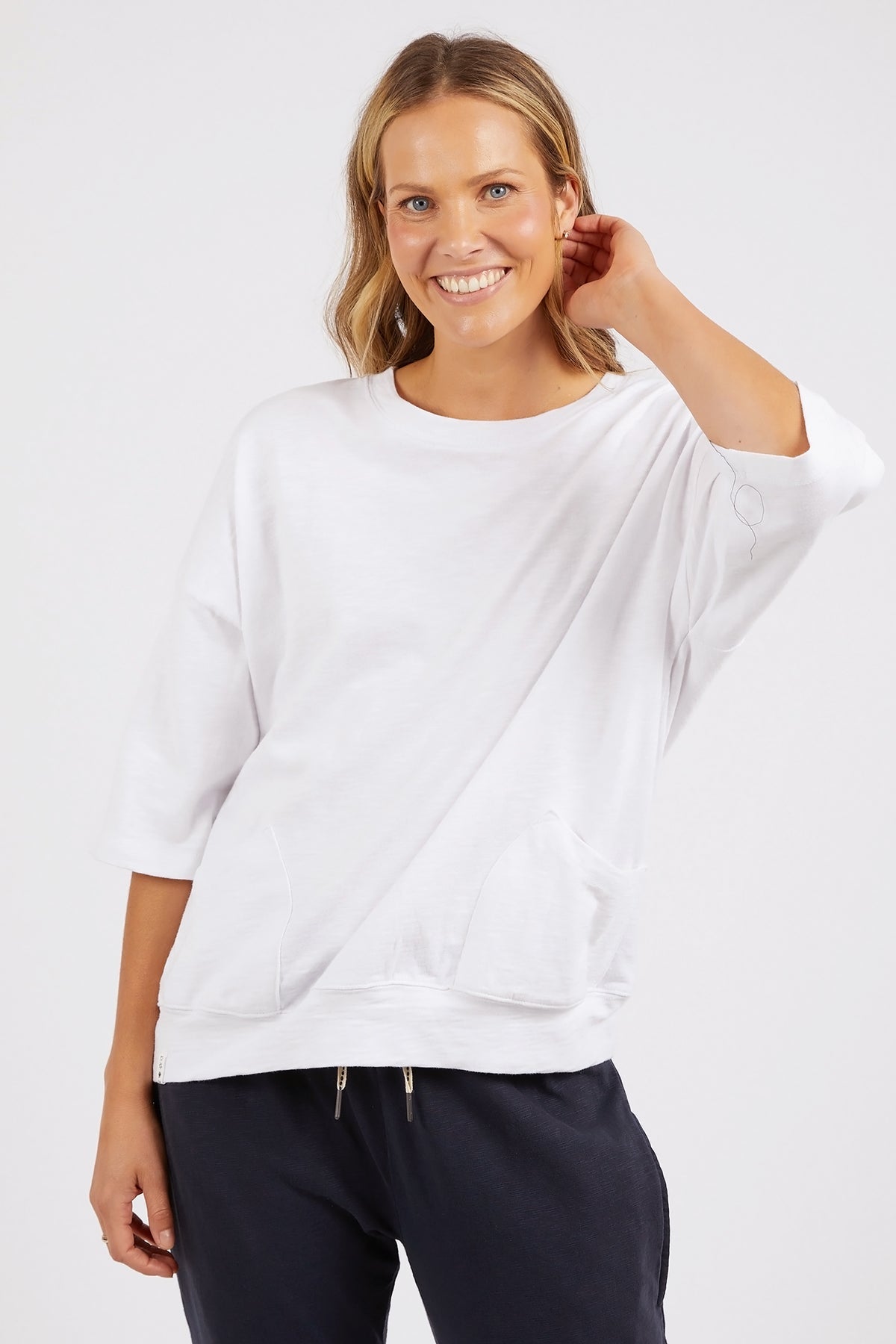 Woman wearing a white oversized sweater and dark pants on a light background