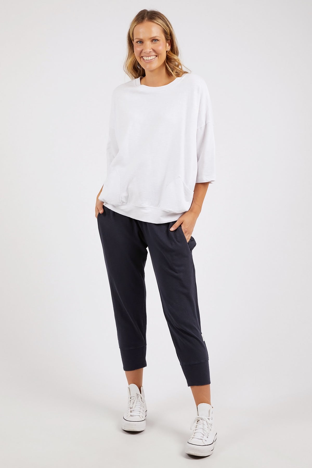 Woman wearing a white top and navy pants on a white background