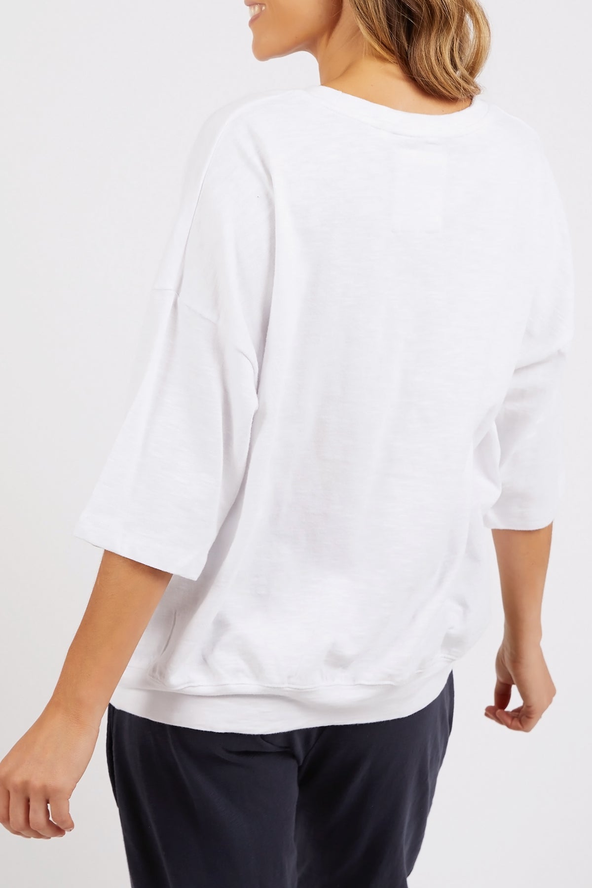 Person wearing a white long-sleeve shirt and dark pants on a plain background