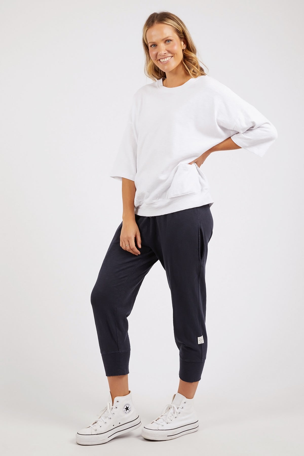 Woman wearing a white oversized shirt and navy jogger pants on a white background