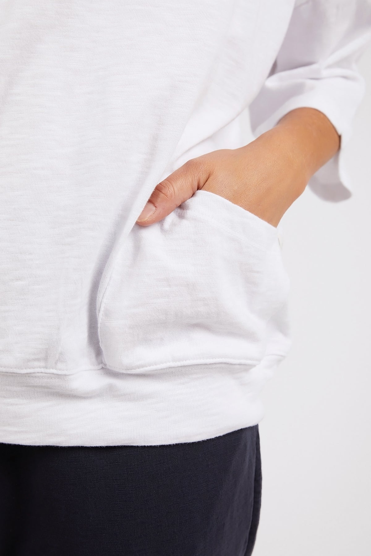 Person wearing a white sweatshirt with a pocket, standing against a plain background