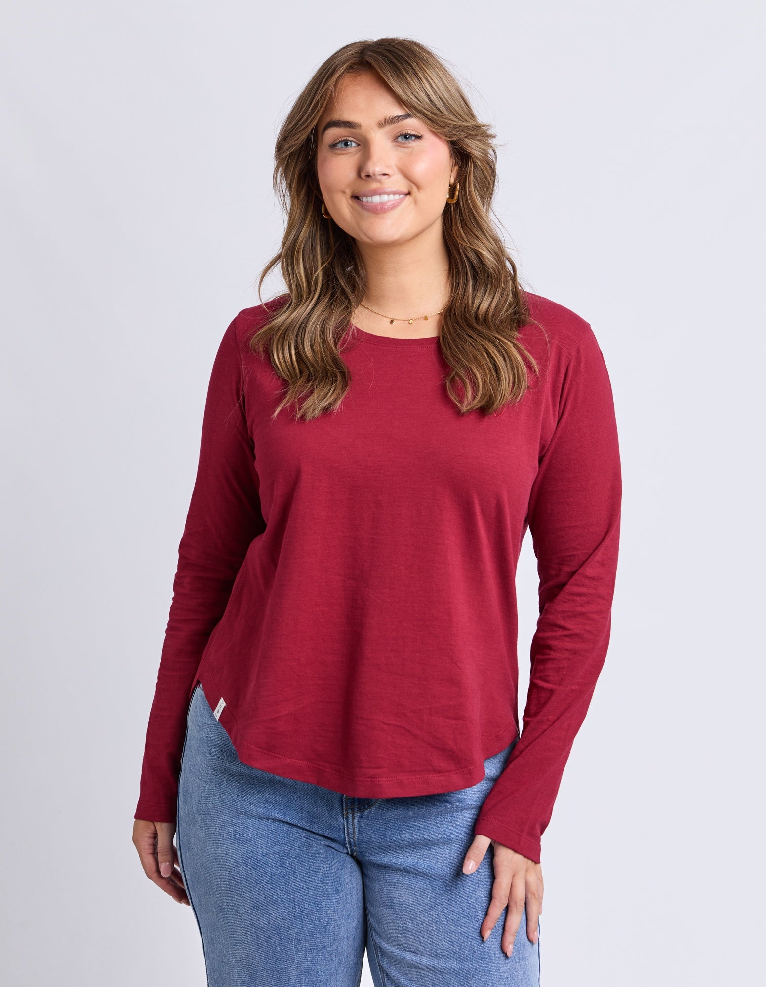 Woman wearing a red long-sleeve shirt and blue jeans on a plain background