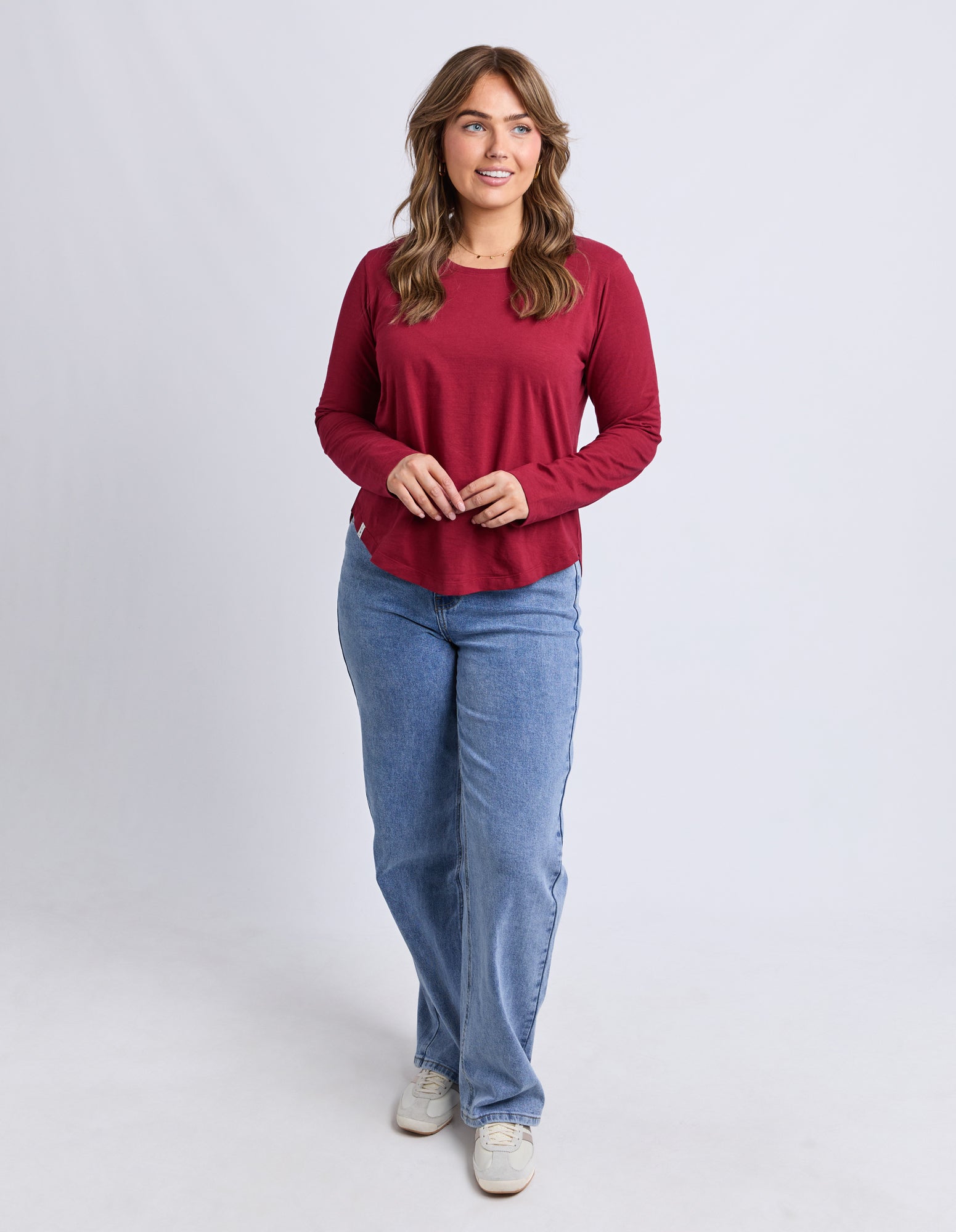 Woman wearing a red long-sleeve top and blue jeans on a white background