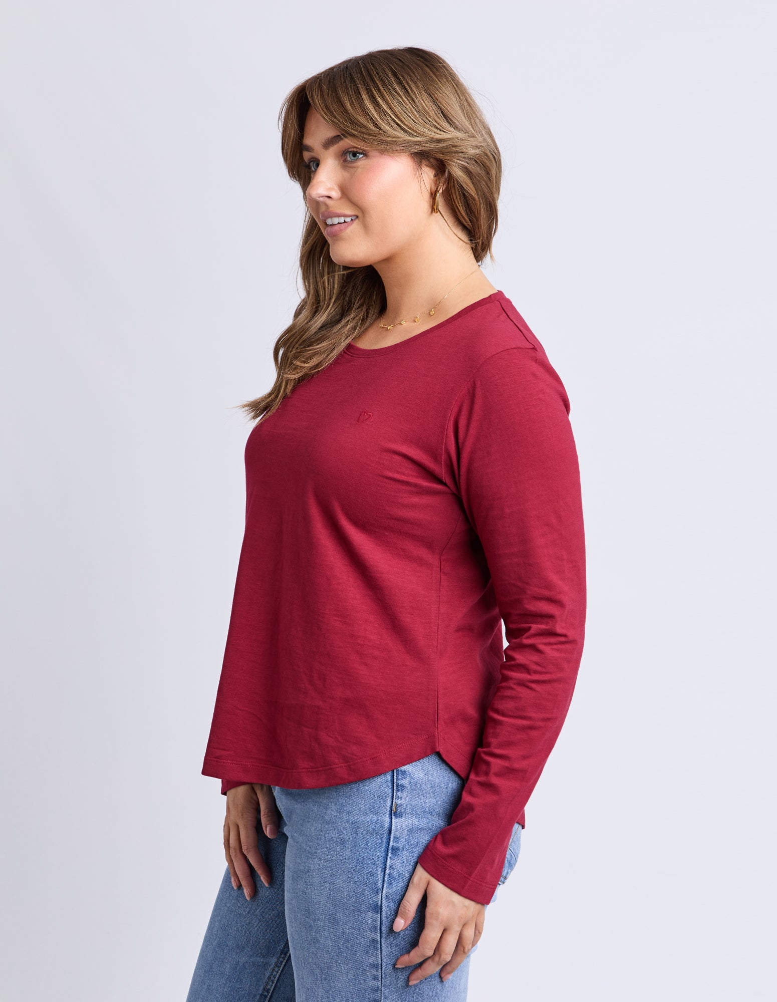 Woman wearing a red long-sleeve top and blue jeans on a white background