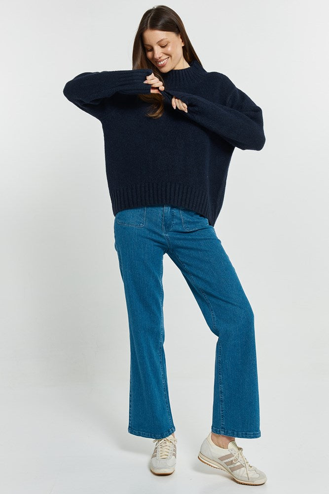 Woman wearing a navy sweater and blue jeans on a white background