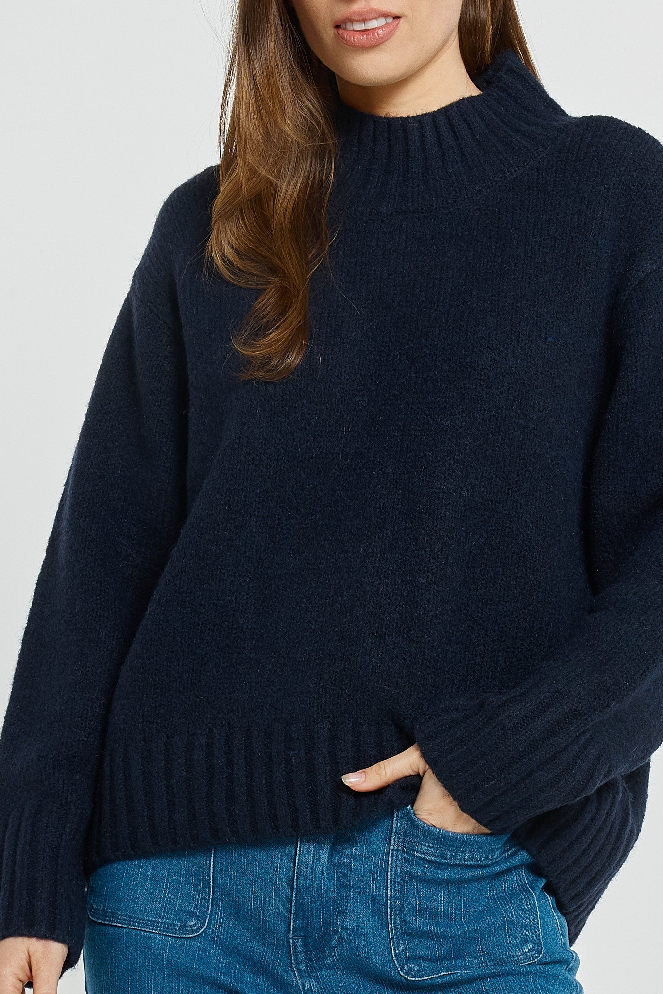 Person wearing a dark blue sweater and blue jeans on a light gray background