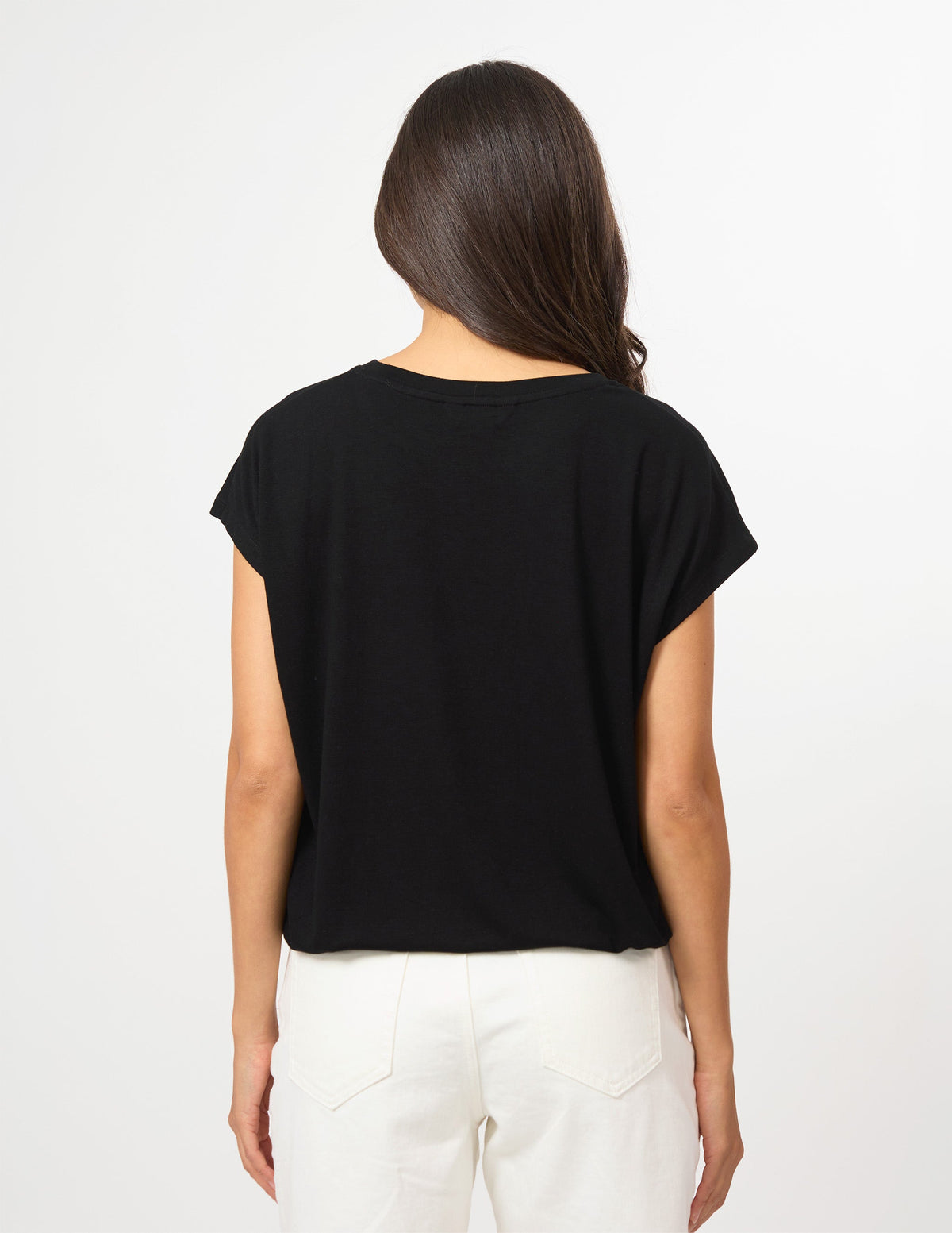 A woman viewed from the back wearing a black short-sleeve crop top and white pants against a plain white background.