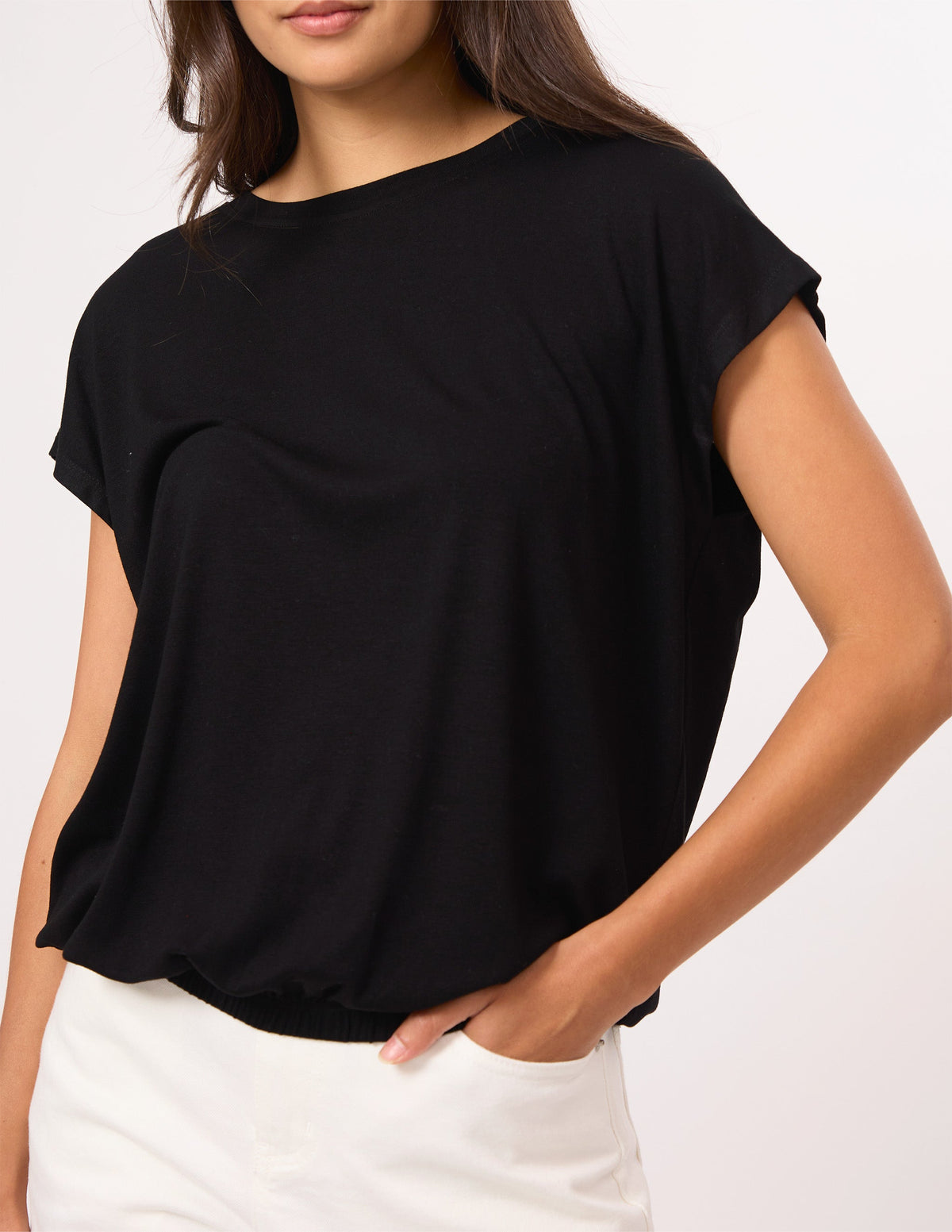 A woman wearing a black short-sleeve crewneck top and white pants, cropped from the mouth down against a plain light background.