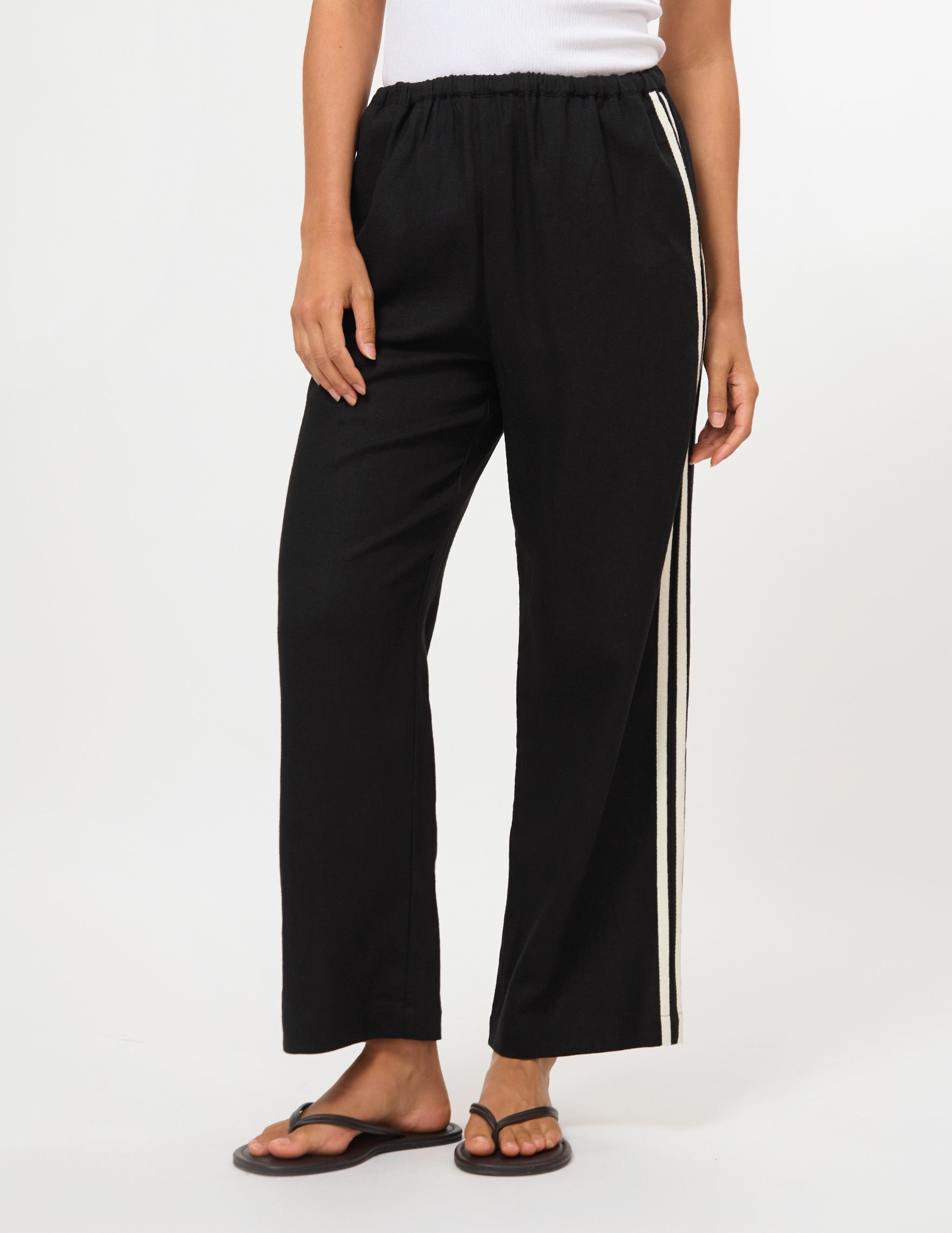 Black wide-leg cropped pants with a white side stripe, modeled with a white top and black flip-flops against a white studio background.