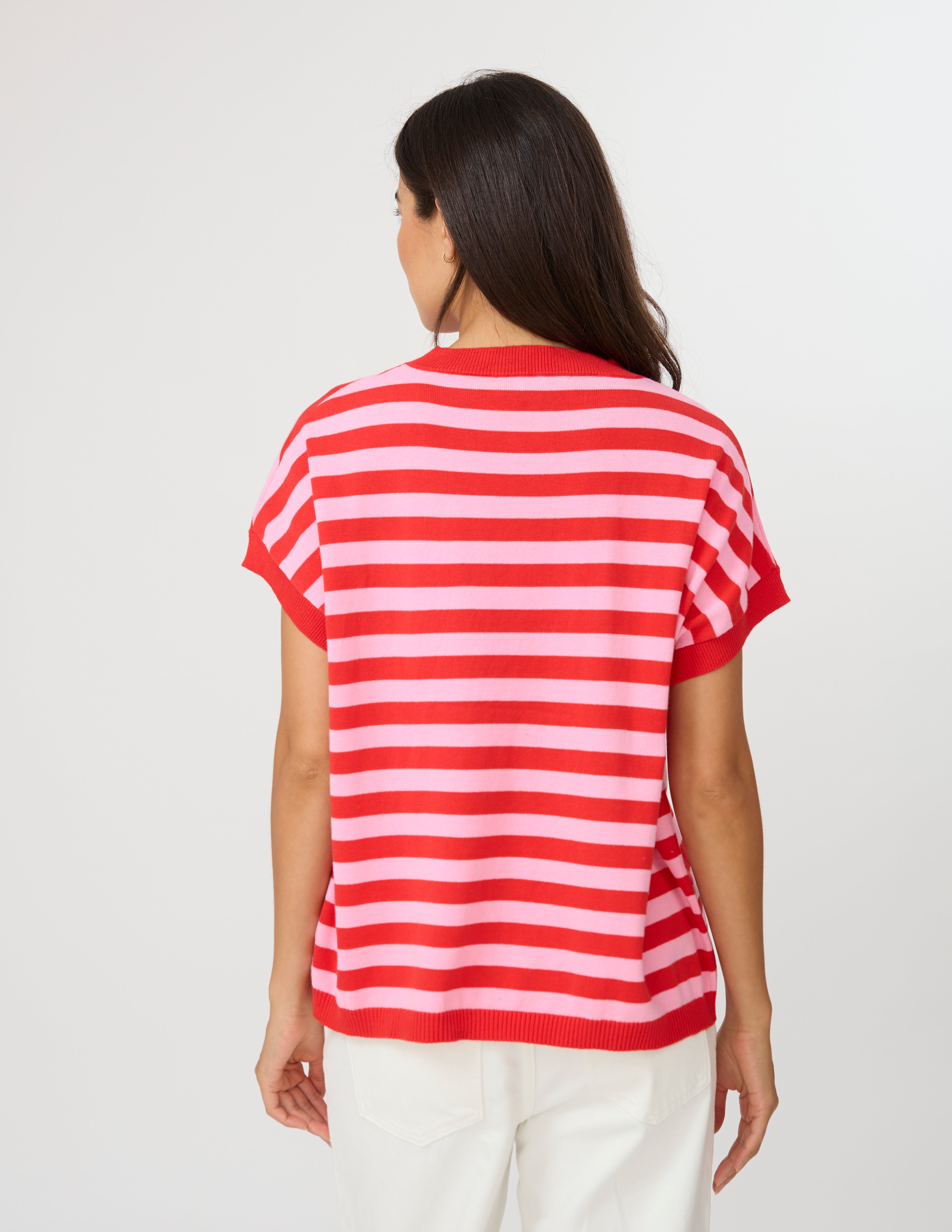 A woman viewed from the back wearing a red and white horizontally striped short-sleeve top and white pants, against a plain light gray studio background.